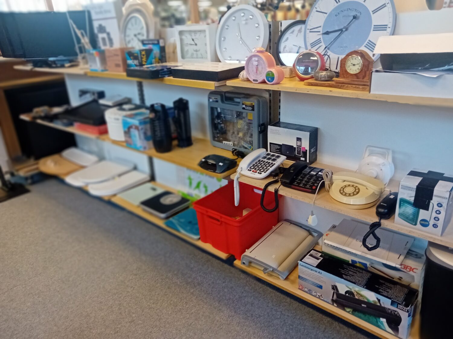 Een overzicht van kantoorbenodigdheden, telefoons, klokken en andere accessoires op een houten plank, geschikt voor kantoor- of winkelomgeving.