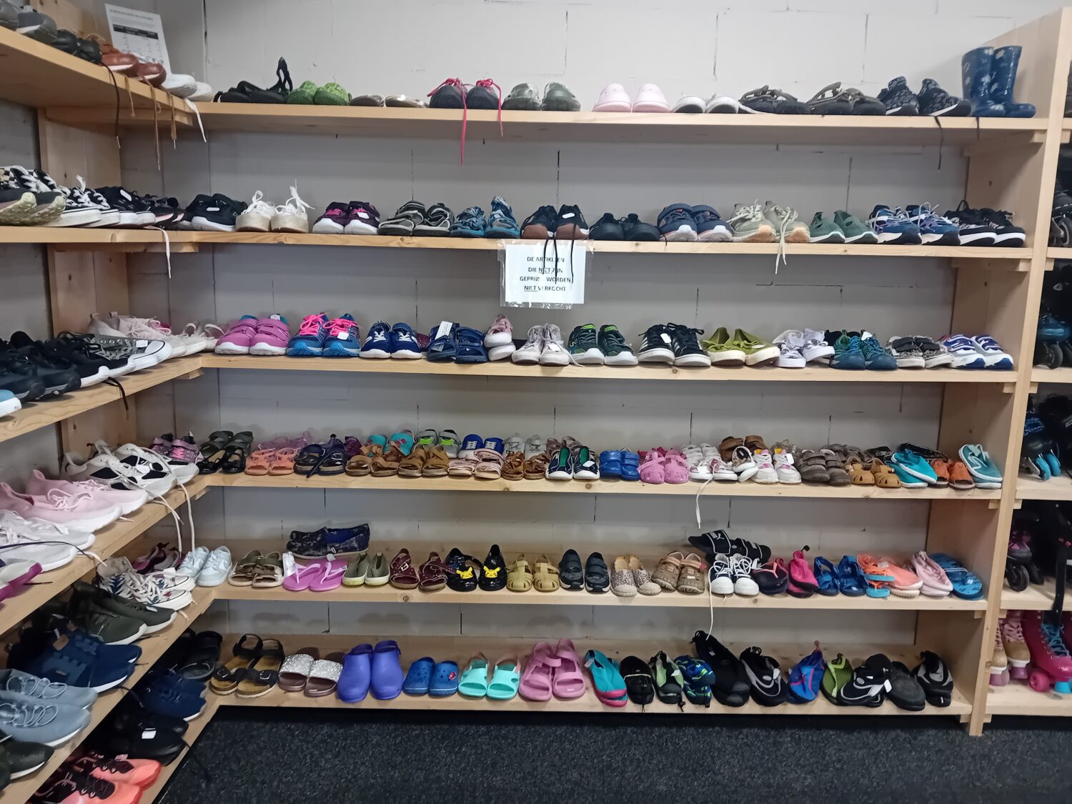 Een overzicht van diverse kinderschoenen en sneakers op houten rekken, beschikbaar bij Dorcas, geschikt voor verschillende leeftijden en stijlen.