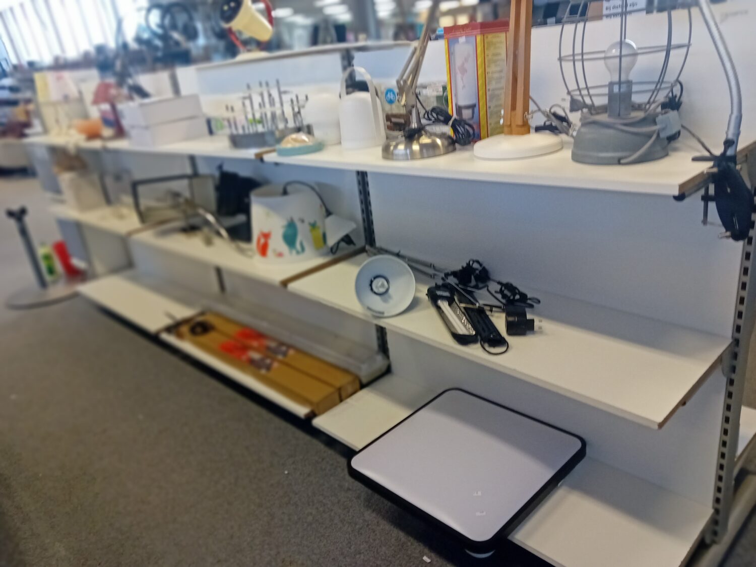 Een overzicht van een werkplek met verschillende kantoorartikelen, zoals lampen, telefoons, en een weegschaal, geschikt voor zakelijke of thuiswerkomgevingen.