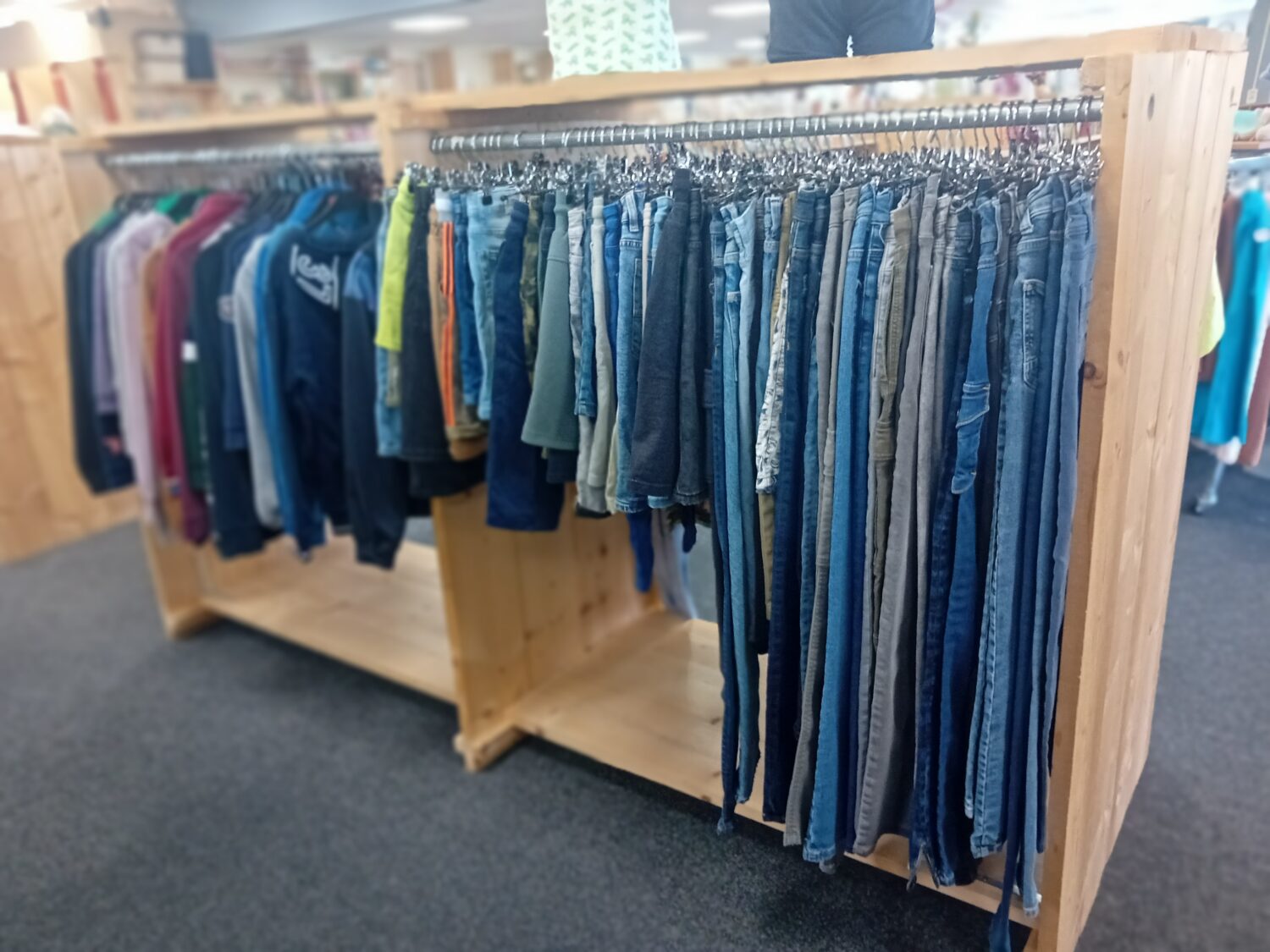 Een kledingrek met een assortiment aan jeans en shirts, geschikt voor hergebruik en duurzame mode, te vinden bij Dorcas.
