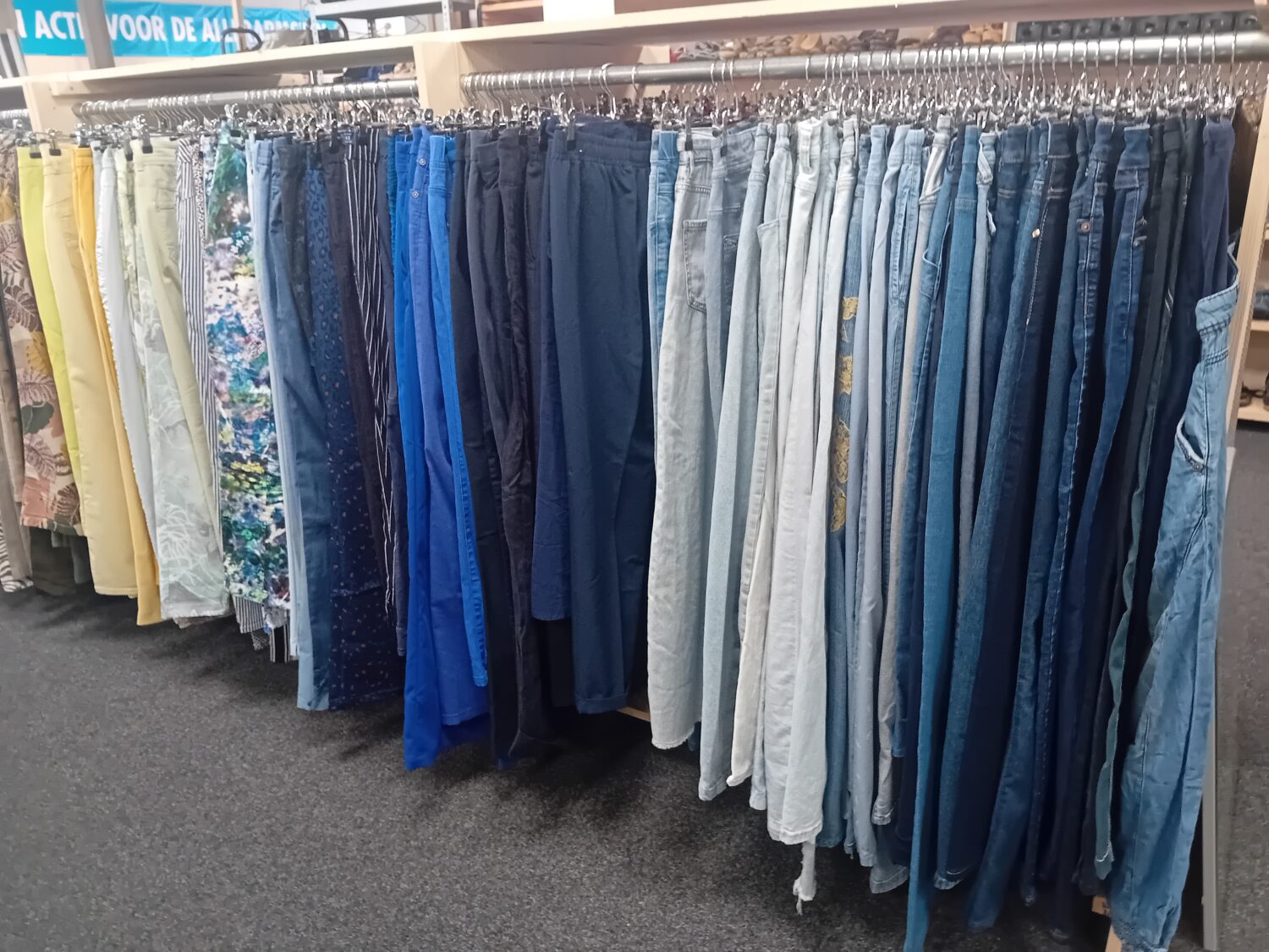 Een overzicht van verschillende soorten blauwe spijkerbroeken en jeanshosen op een winkelrek, geschikt voor hergebruik en duurzame mode.