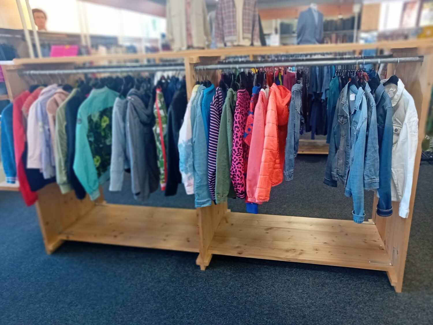 Kinderkleding op een houten kledingrek in een winkel, geschikt voor kinderen van verschillende leeftijden, met diverse kleuren en stijlen, ideaal voor tweedehands of goede doelen winkels.