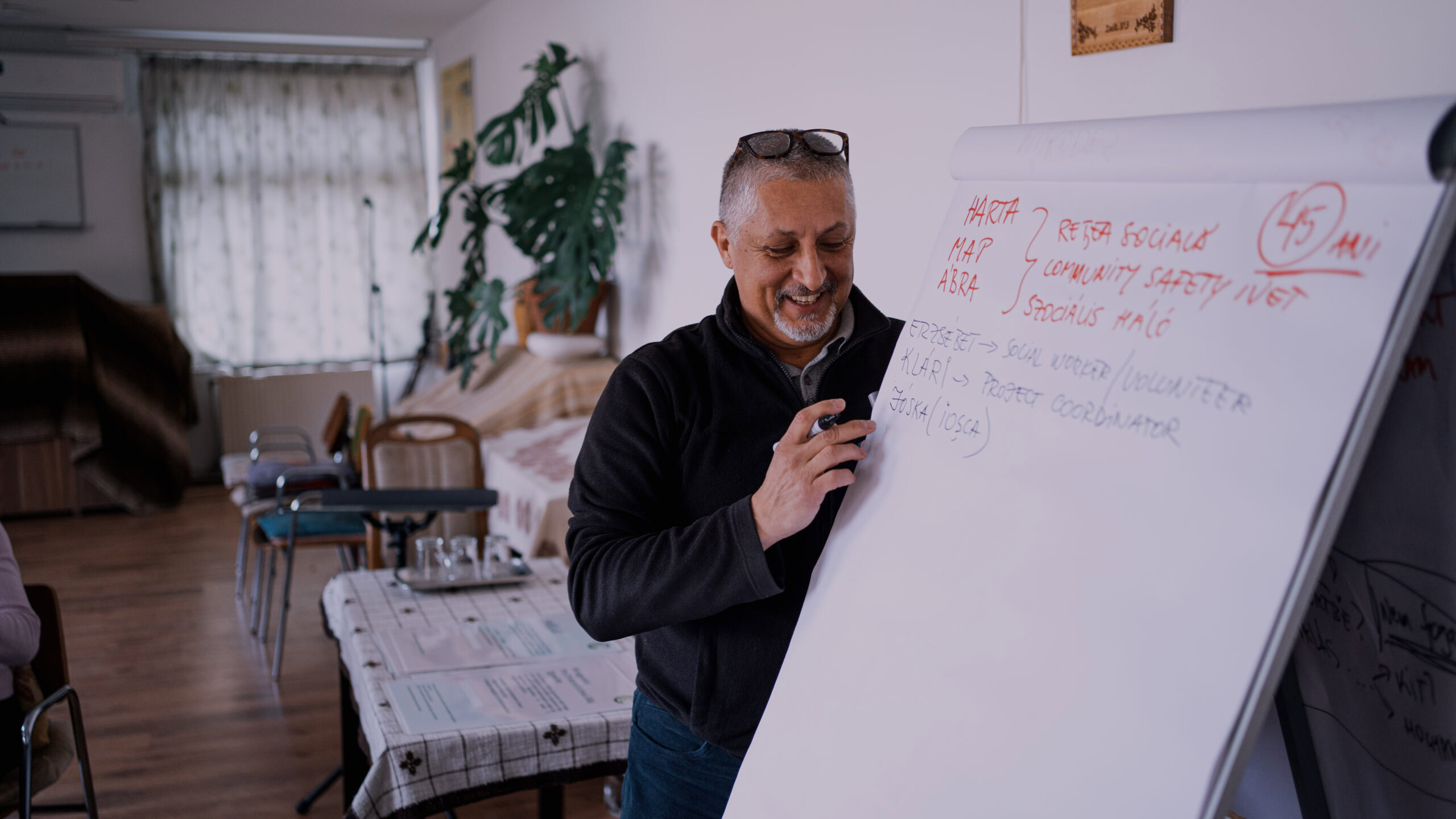 Man die glimlachend op een whiteboard schrijft tijdens een bijeenkomst over schenken met belastingvoordeel.