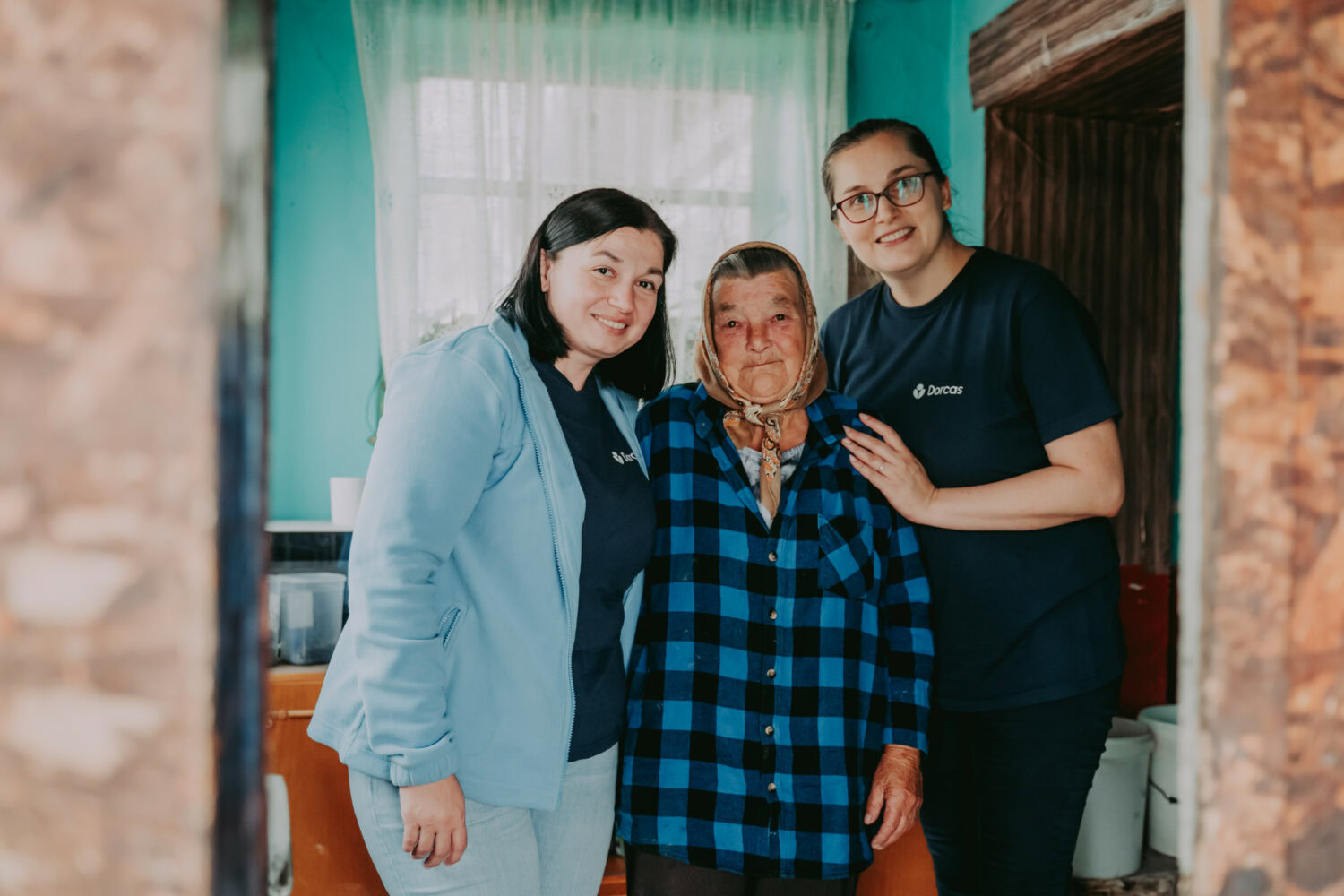 Hulpverleners van Dorcas bieden ondersteuning aan een oudere vrouw in haar huis, onderstrepend de christelijke missie van het goede doel.
