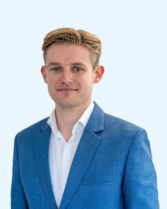 Een professioneel portret van een man in een blauwe jas en witte overhemd, geschikt voor zakelijke en personeelsgerelateerde doeleinden.