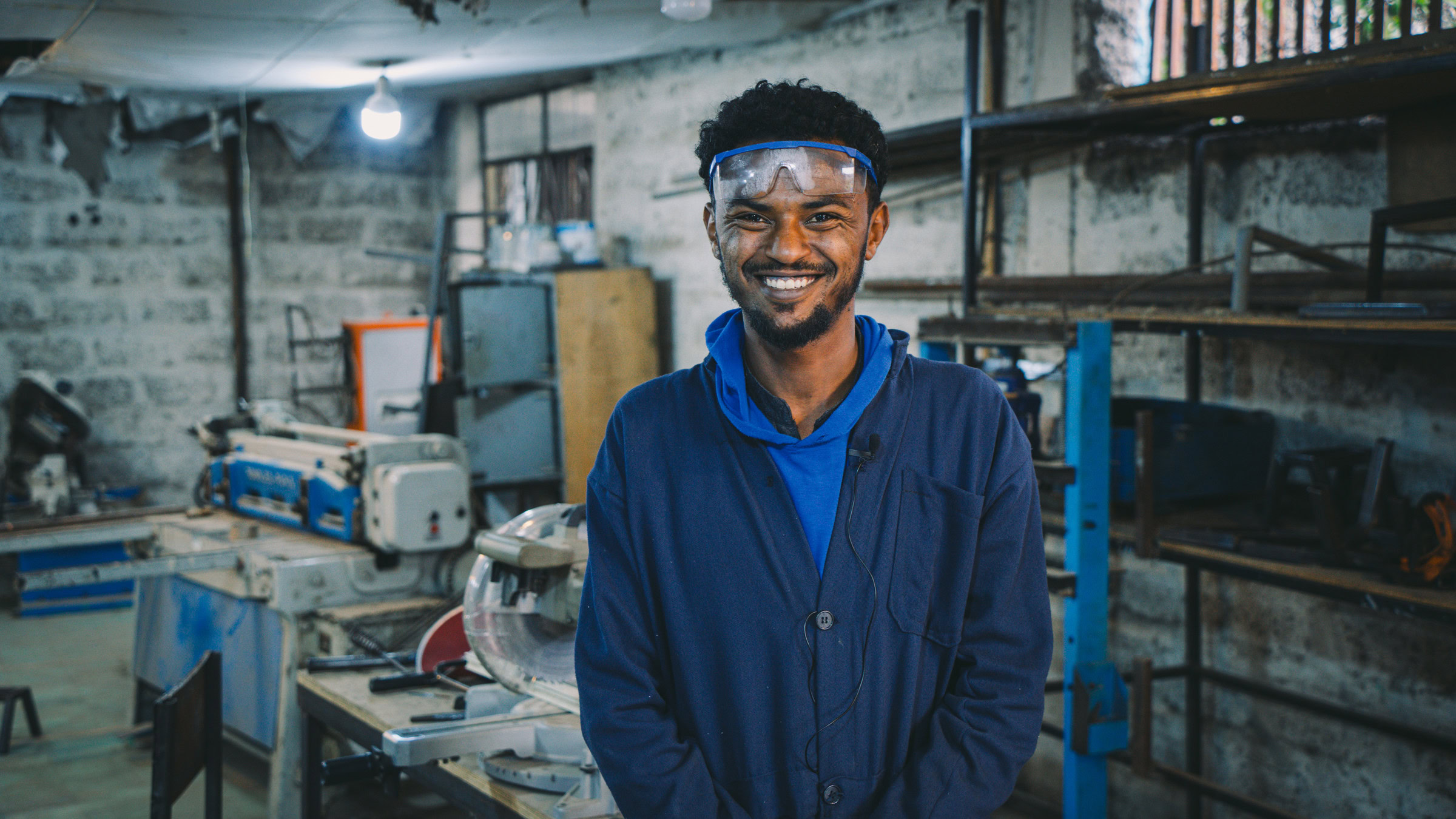 Een glimlachende man in een werkplaats met machines en gereedschap, passend bij de categorie 'Bedrijven' op.