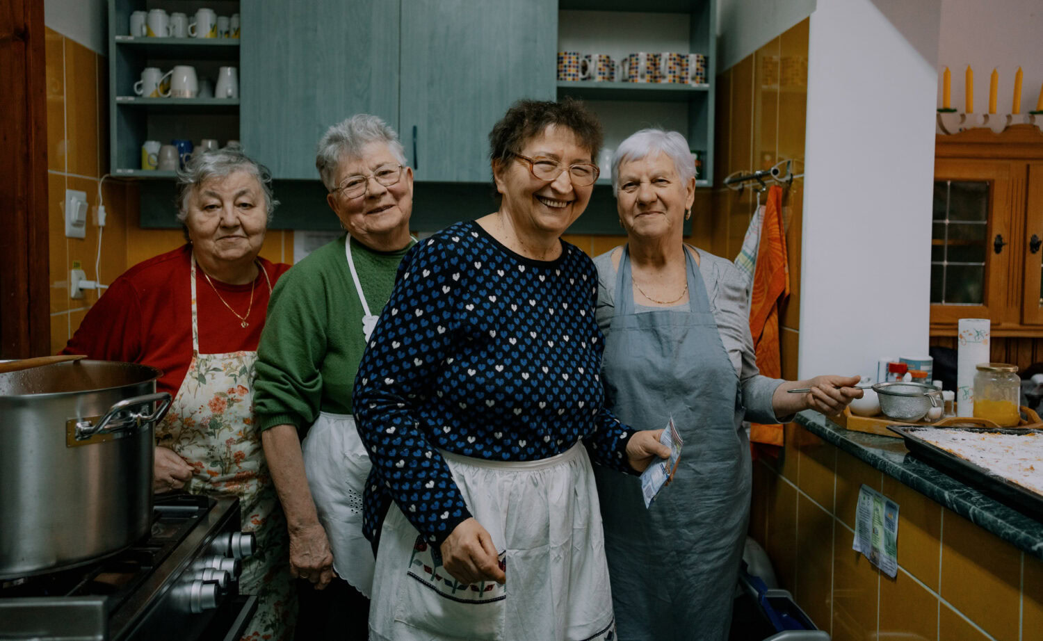 Gezellige groep ouderen vrouwen die lachen in een keuken, actief betrokken bij gemeenschapsactiviteiten en ondersteuning, passend bij de context van 'Wat we doen'.