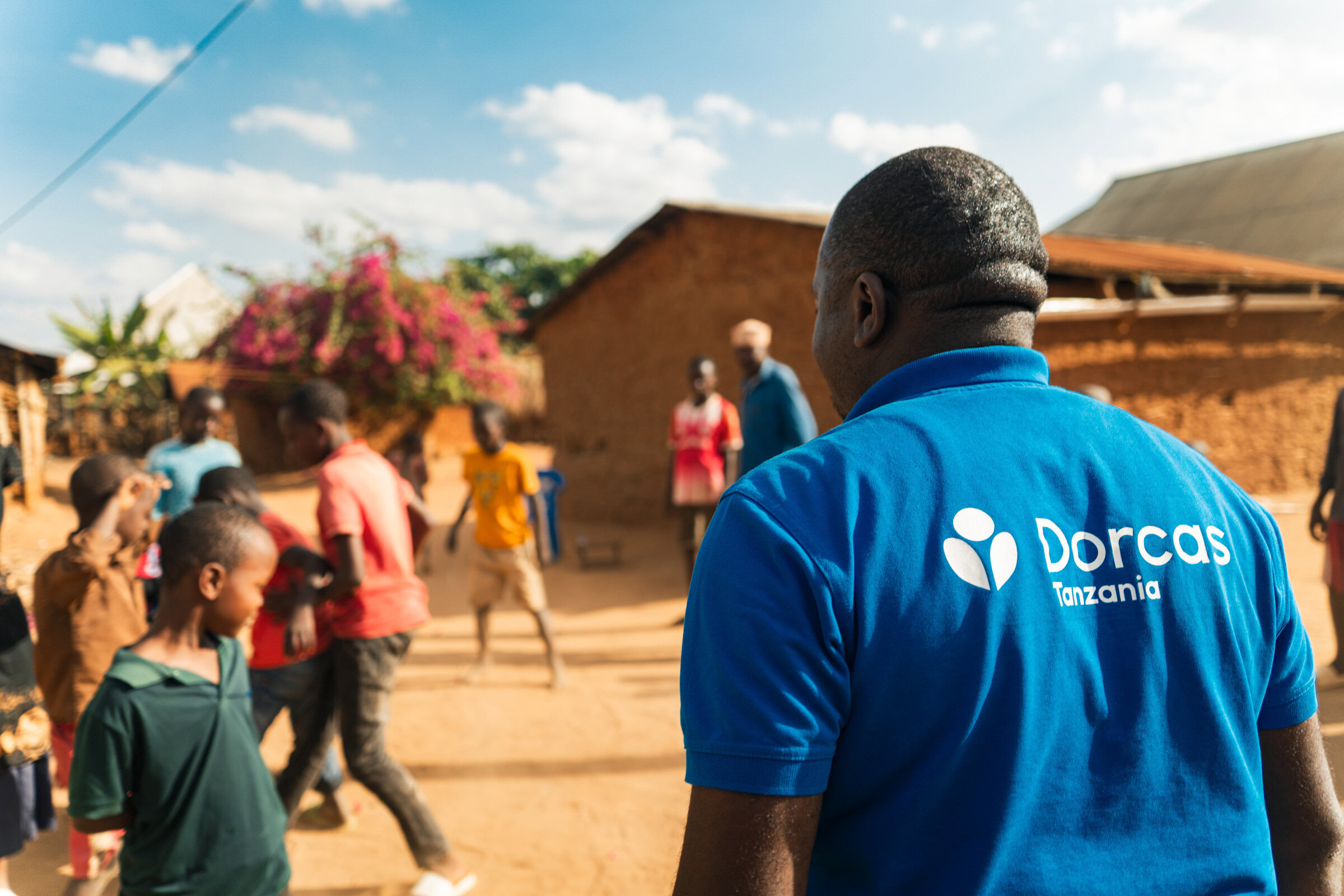 Een Dorcas-medewerker in Tanzania biedt ondersteuning aan lokale gemeenschappen, met kinderen en volwassenen die deelnemen aan een hulpactie in een Afrikaans dorp.