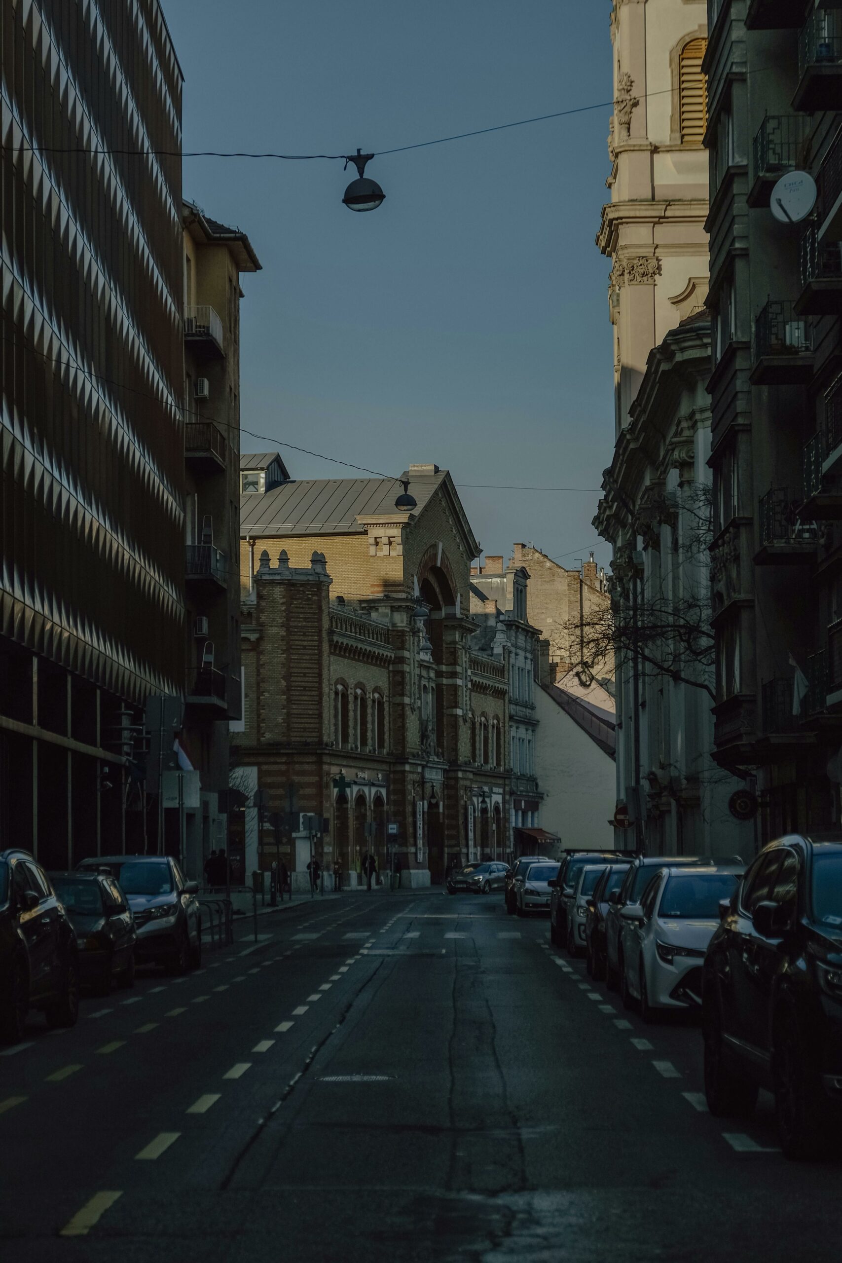 Een smalle straat met oude gebouwen en geparkeerde auto's, onder een heldere blauwe hemel, symboliseert stedelijke bescherming en veiligheid.