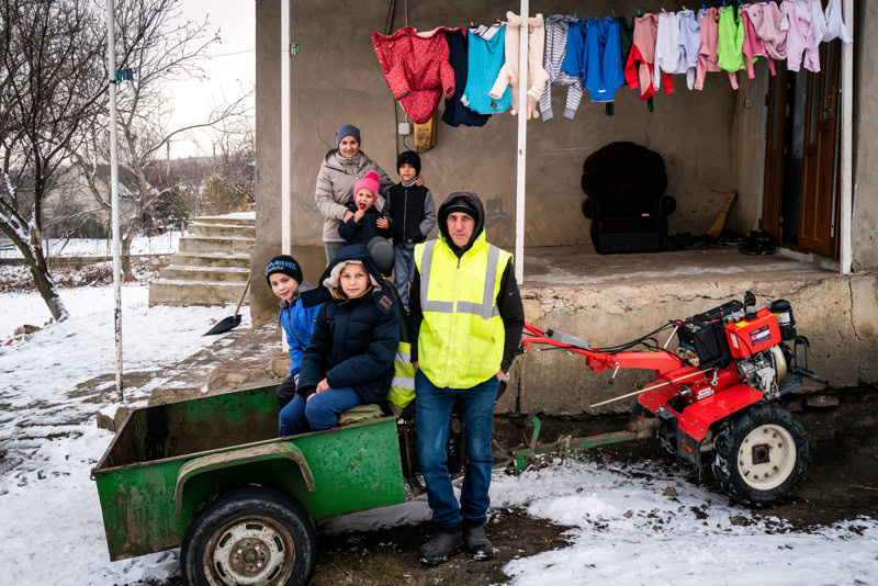Vrijwilligers en kinderen in Moldavië bij hulpactie, met wasgoed en een kleine tractor voor transport.