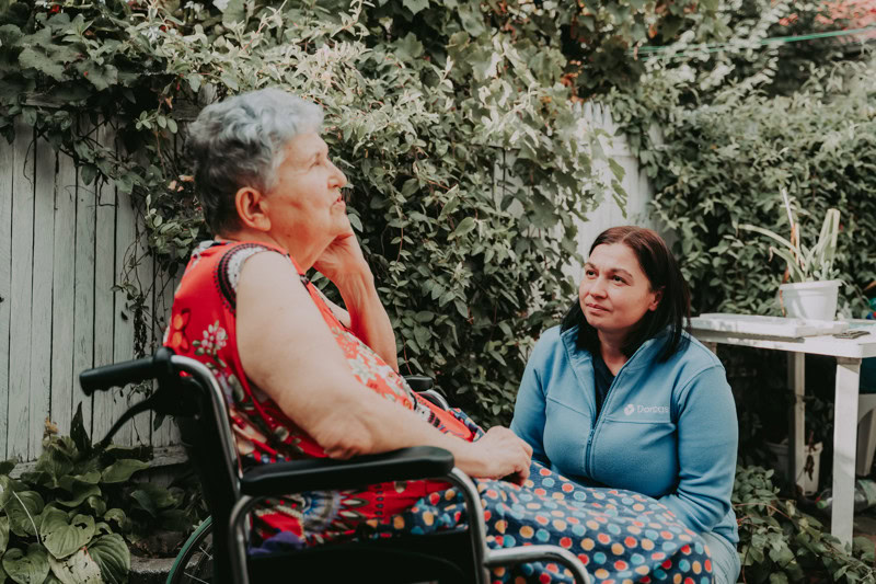 Zorgverlener spreekt met oudere vrouw in tuin, ondersteuning en aandacht voor ouderen in Roemenië.