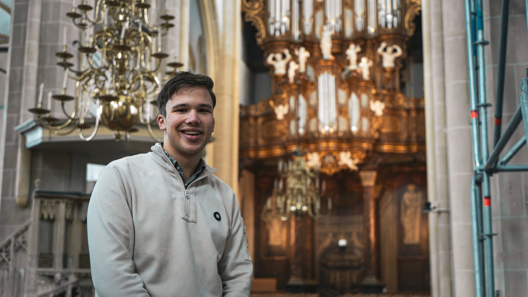 Een jonge man die deelneemt aan de Psalmenmarathon in een kerk, met een warme glimlach en een serene sfeer, omringd door prachtige kerkarchitectuur en kroonluchters.