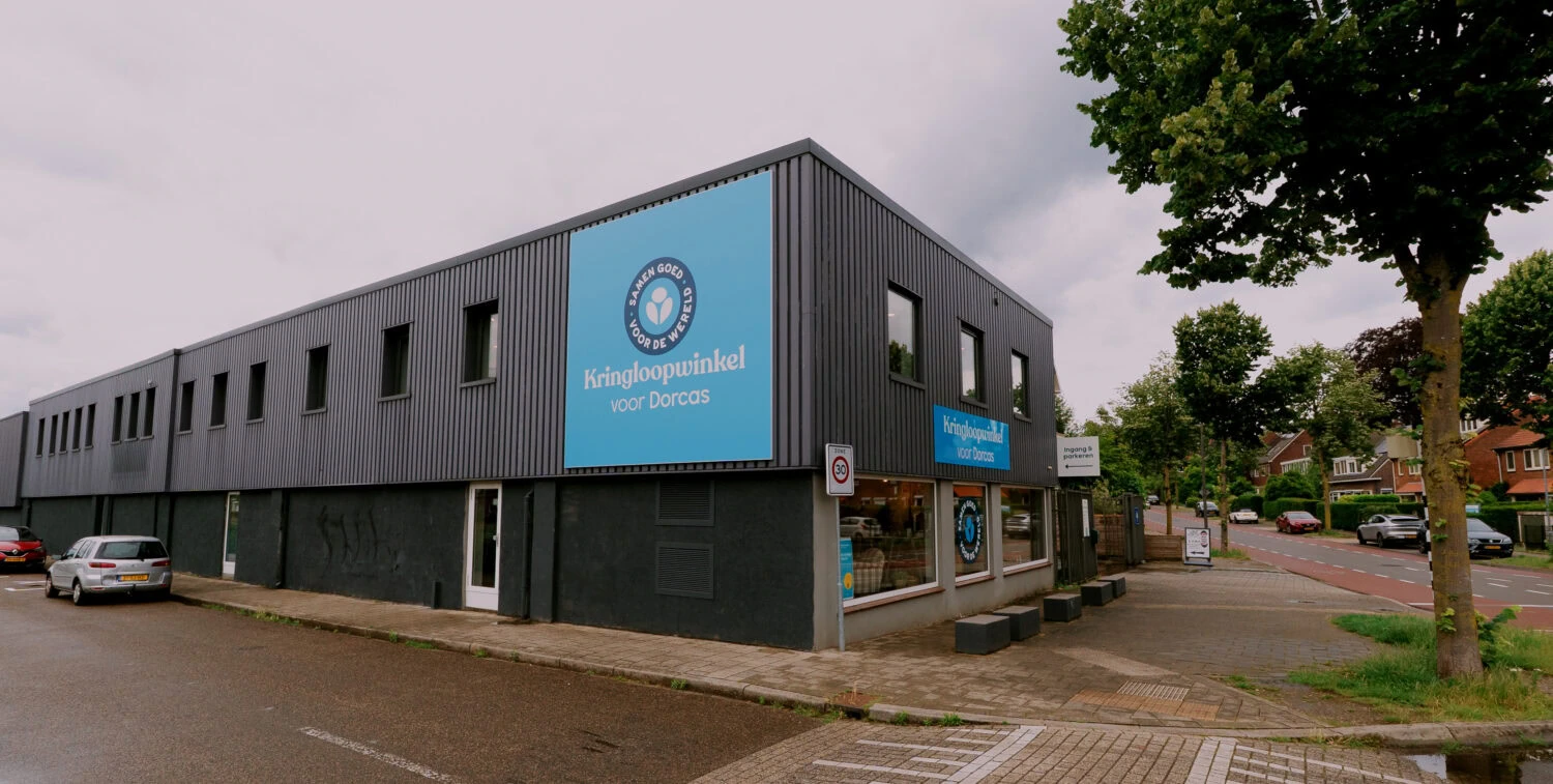 Het Dorcas distributiecentrum in Velp, een gebouw dat humanitaire hulp en armoedebestrijding ondersteunt, met een blauwe logo en een groene omgeving.