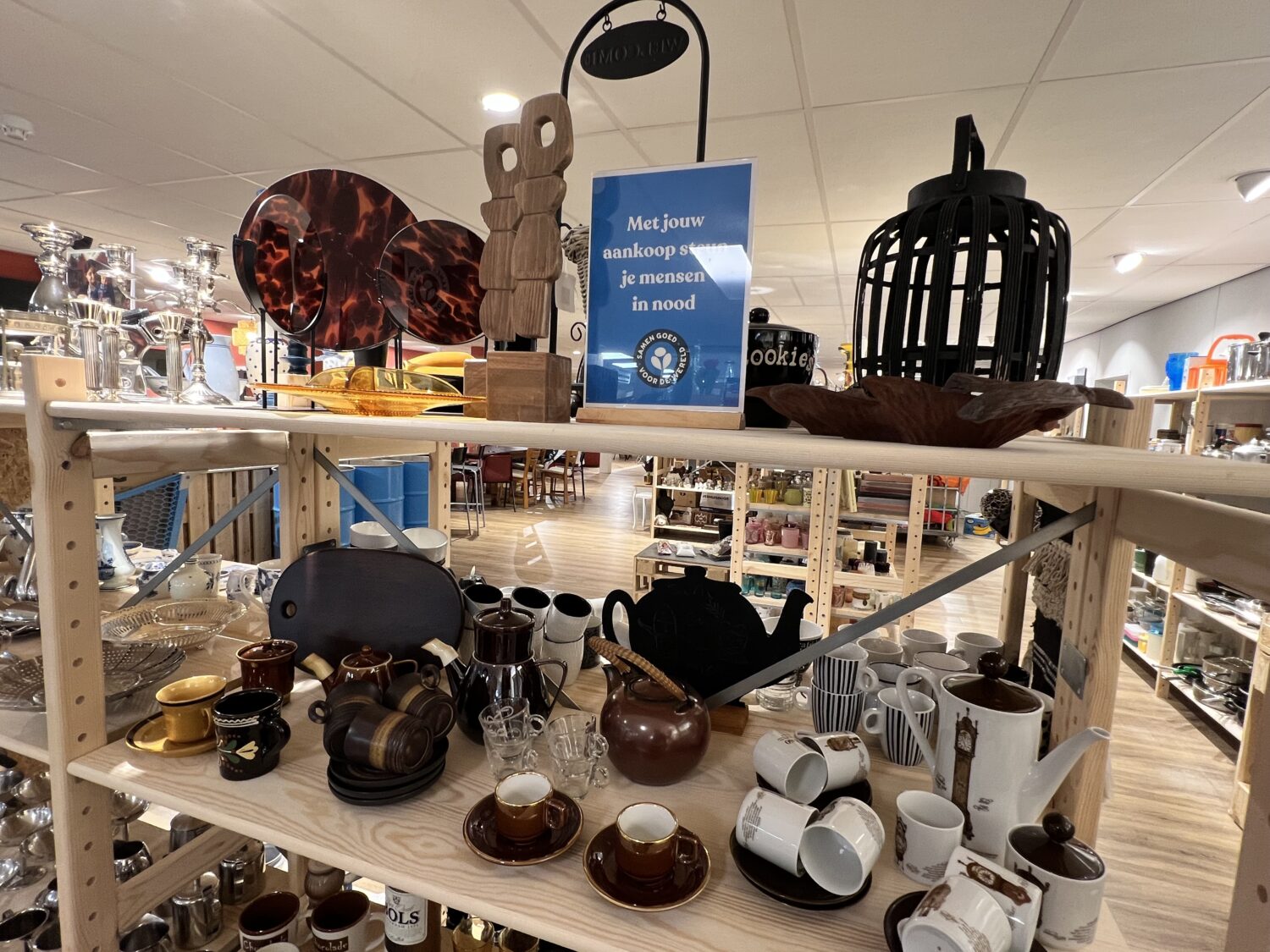 Kleine woonaccessoires en servies, zoals vazen, bekers en decoratieve objecten, uitgestald op een winkelrek in een winkel vol huishoudartikelen en keukengerei.