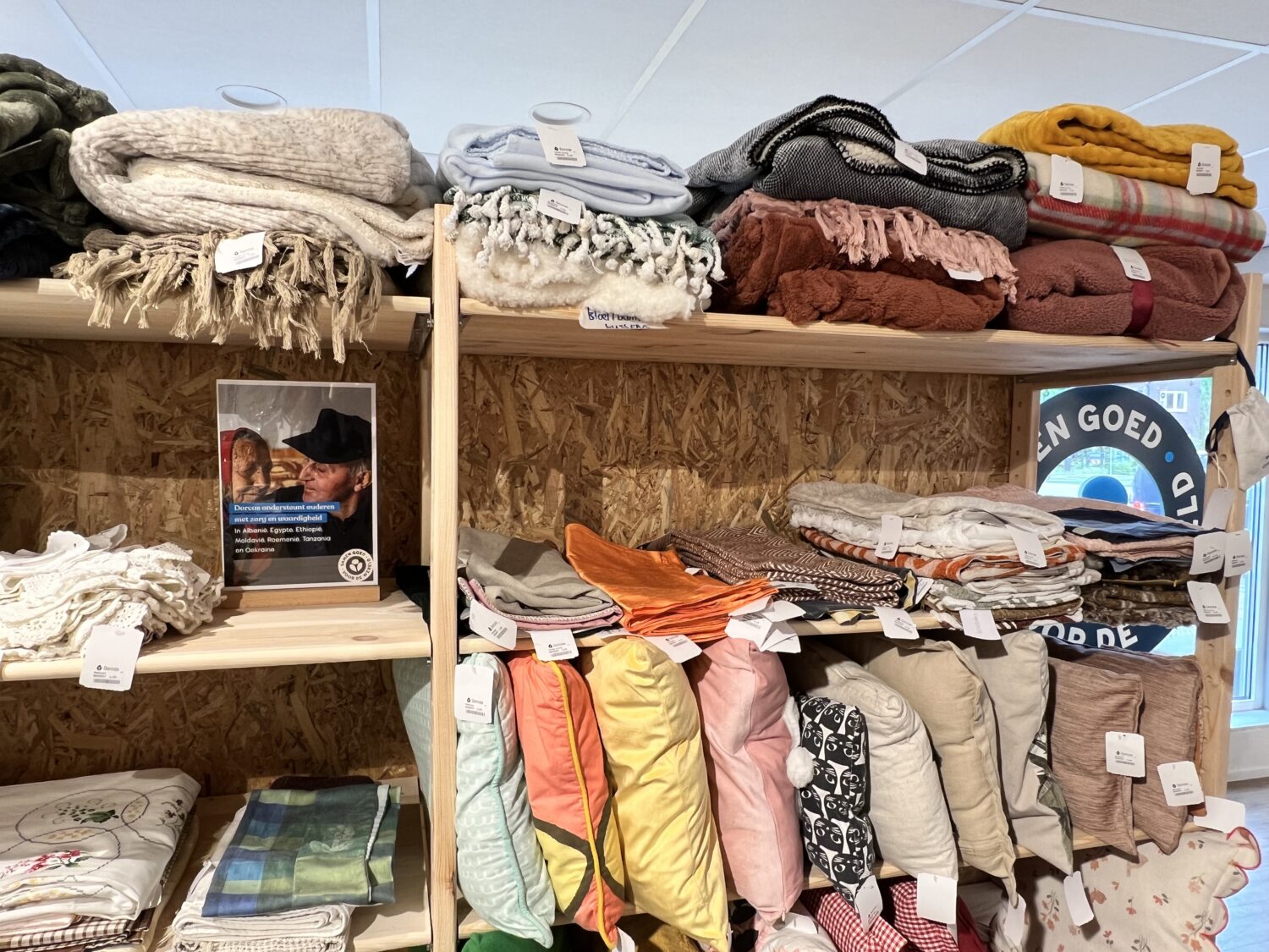 Diverse wollen en sjaals, netjes opgevouwen en uitgestald op houten planken, klaar voor donatie of verkoop bij Dorcas.