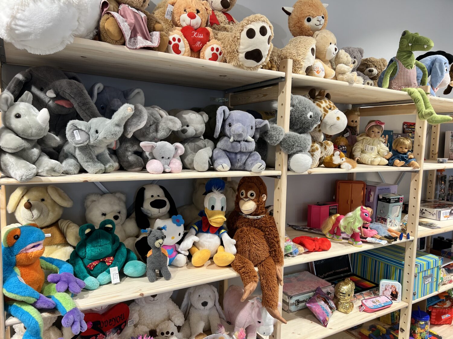 Een assortiment zachte knuffels en speelgoed, waaronder beren, dieren en poppen, uitgestald op winkelrekken, klaar voor verkoop bij Dorcas.