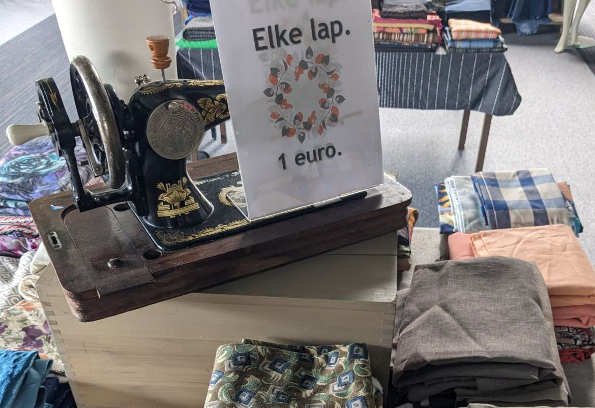 Elke lap, oude naaimachine en gestapelde stoffen voor verkoop bij een tweedehandswinkel of markt.