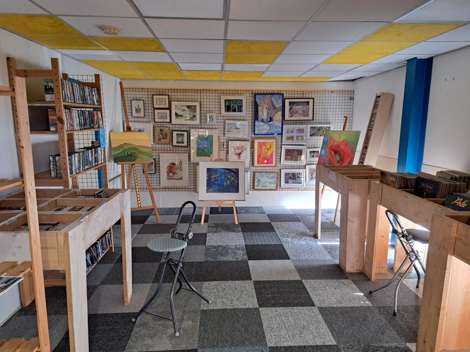 Interieur van een kunstgalerie met schilderijen en kunstwerken aan de muur, houten meubels en stoelen, een gezellige en creatieve sfeer, geschikt voor kunstliefhebbers en exposities.