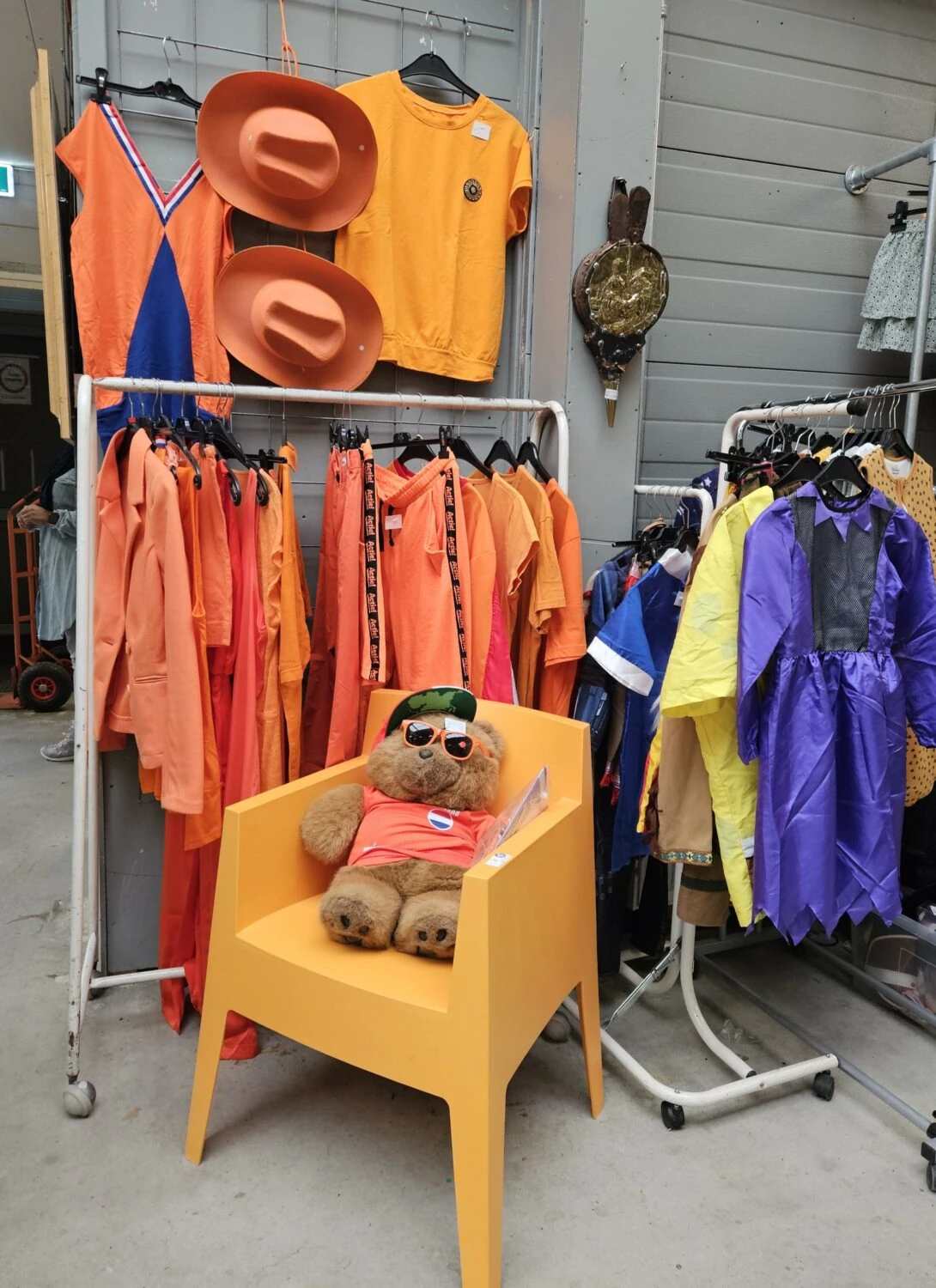 Diverse kinderkleding en accessoires in een winkel, inclusief een teddybeer op een gele stoel, geschikt voor humanitaire hulp en armoedebestrijding in ontwikkelingslanden.