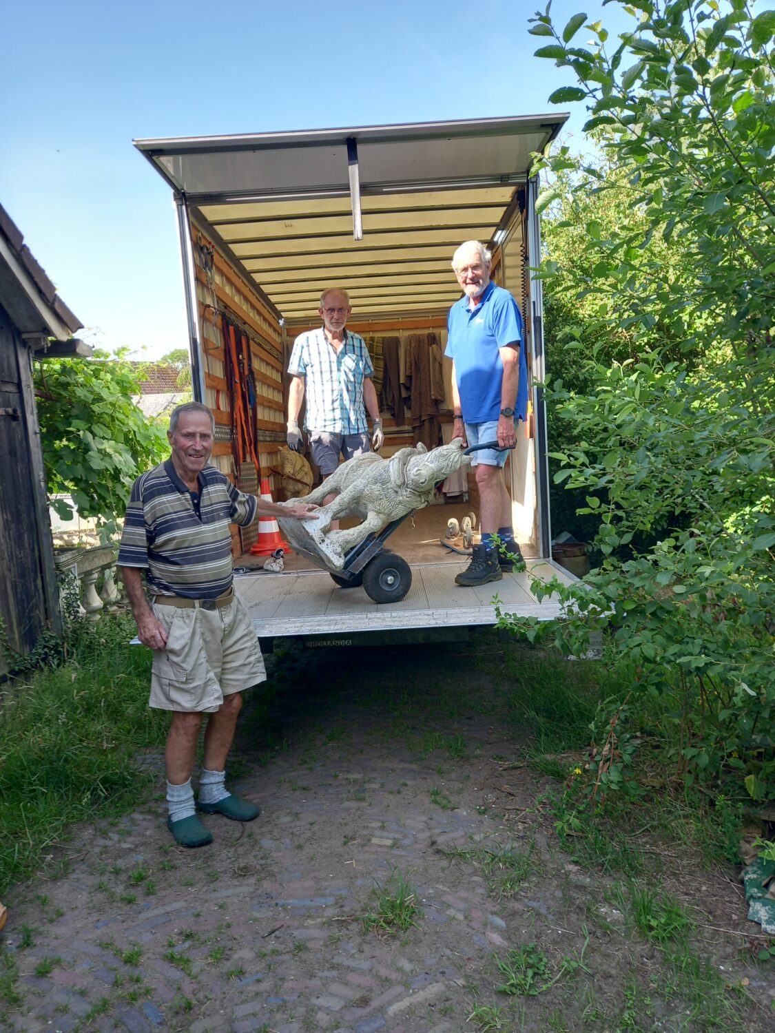Drie mannen bij een verhuiswagen met een betonnen beeld, klaar voor hulpactie in Oost-Europa, benadrukt humanitaire hulp en armoedebestrijding.