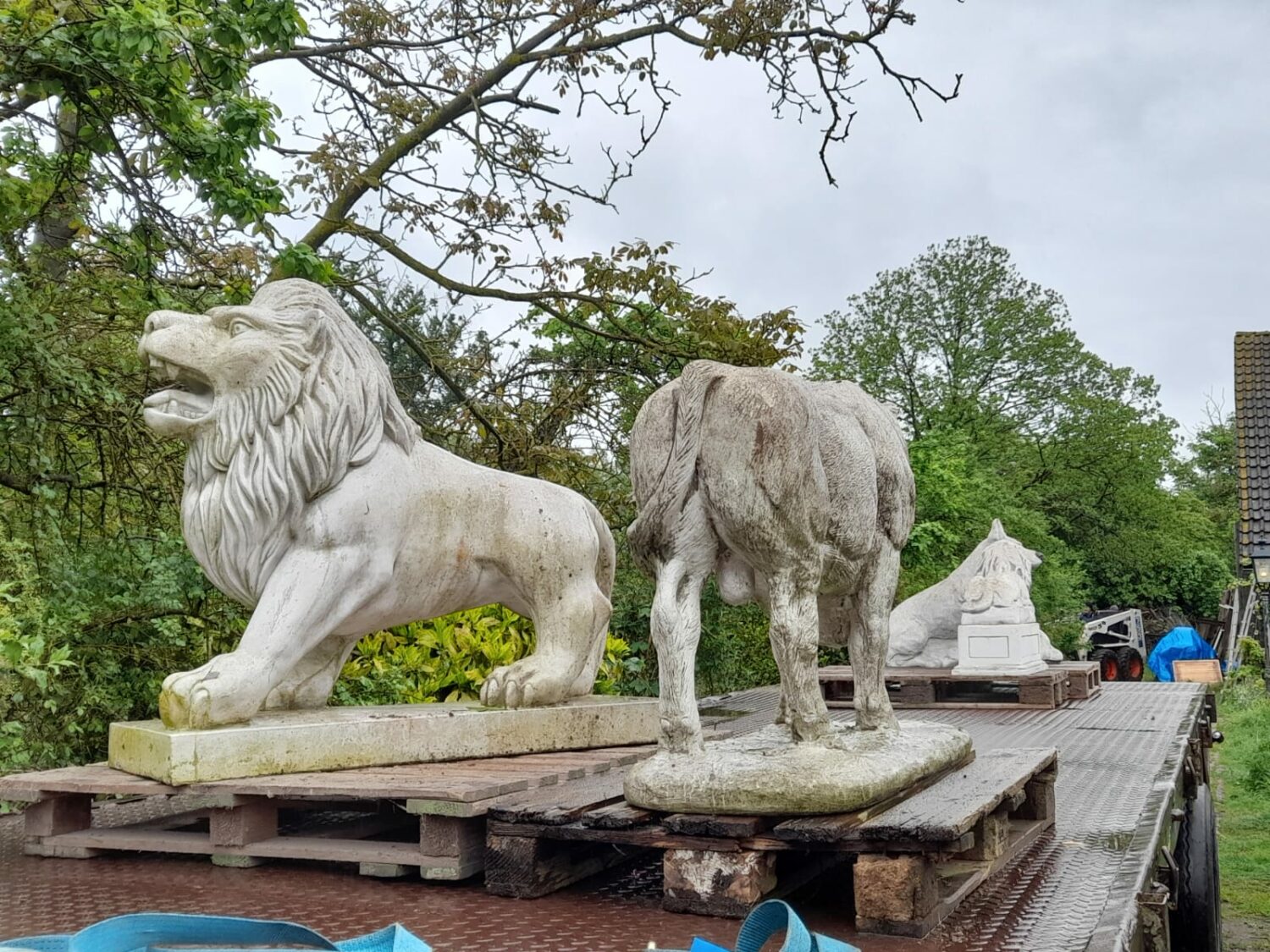 Betonnen dierenbeelden, waaronder een leeuw en een olifant, geplaatst op een houten platform in een groene omgeving, symboliseren kracht en zorg voor de gemeenschap.