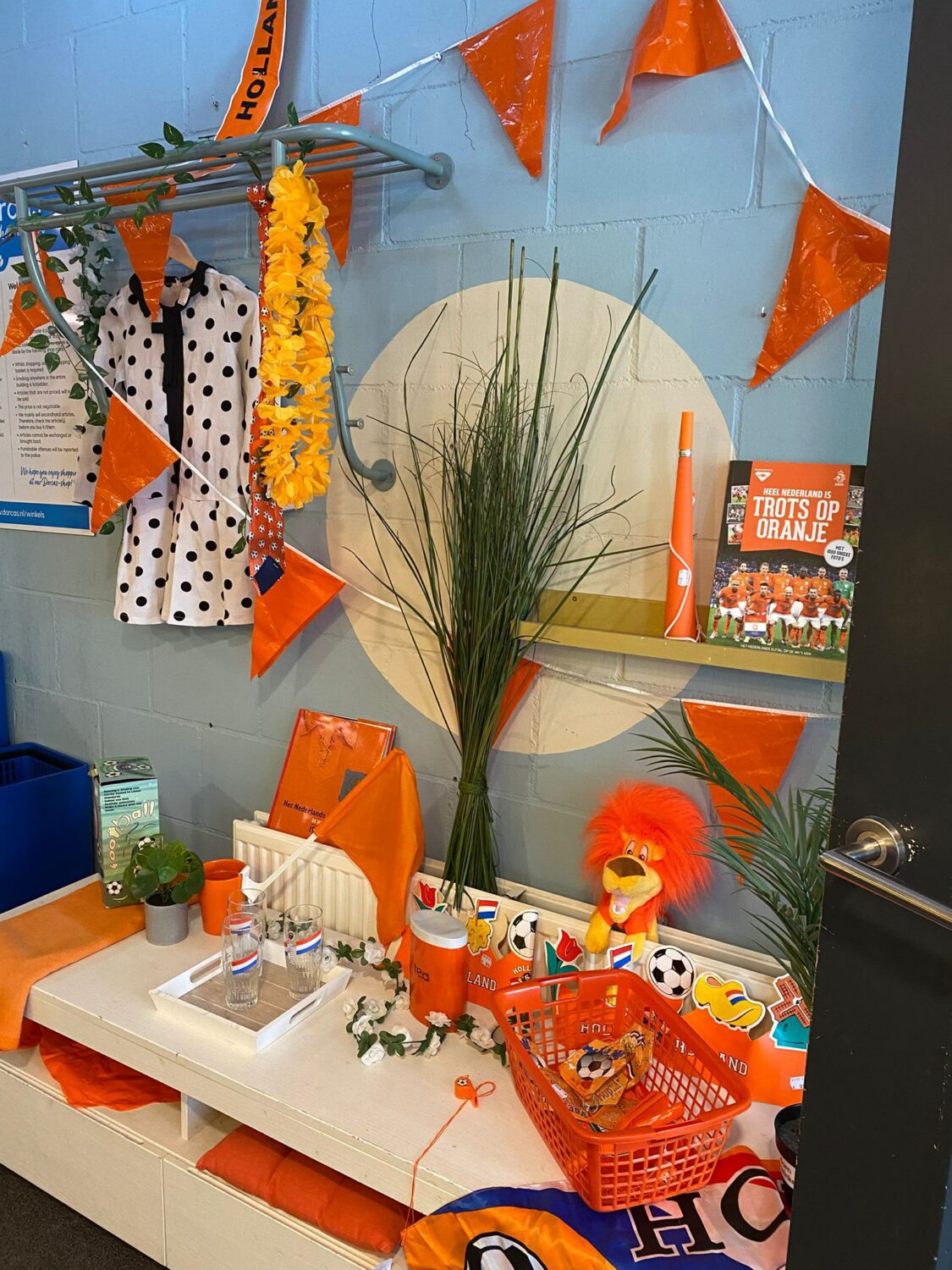 Een feesthoek met oranje decoraties, een tafel met speelgoed en feestartikelen, en een decoratief bloemstuk, klaar voor een verjaardagsfeest of viering.