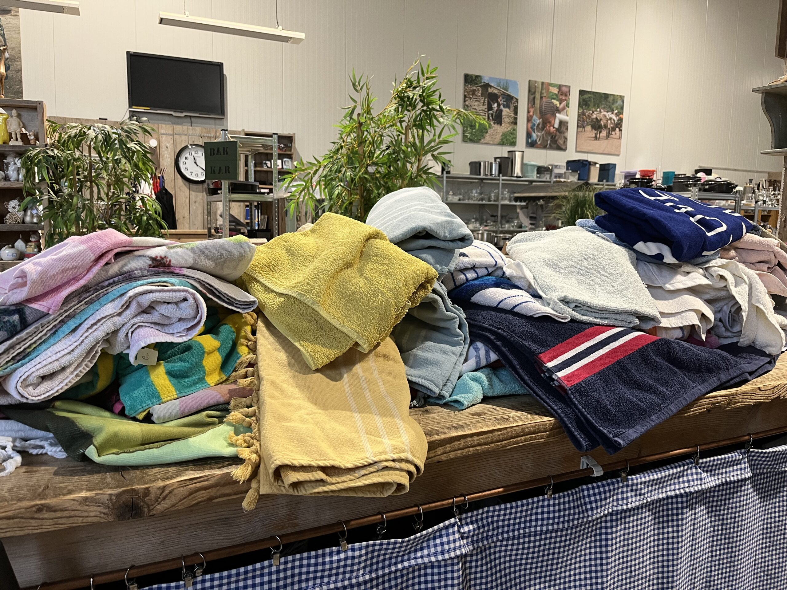 Een tafel vol met opgevouwen handdoeken, badjassen en kleding in verschillende kleuren, klaar voor donatie of verkoop in een tweedehandswinkel of kringloopwinkel.