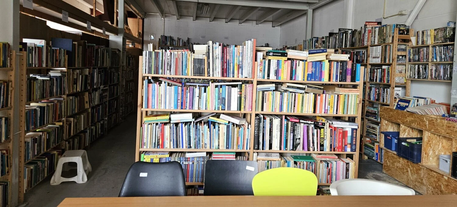 Boekenkast vol met diverse boeken in een bibliotheek of boekwinkel, geschikt voor educatie en kennisdeling, met een tafel en stoelen op de voorgrond.