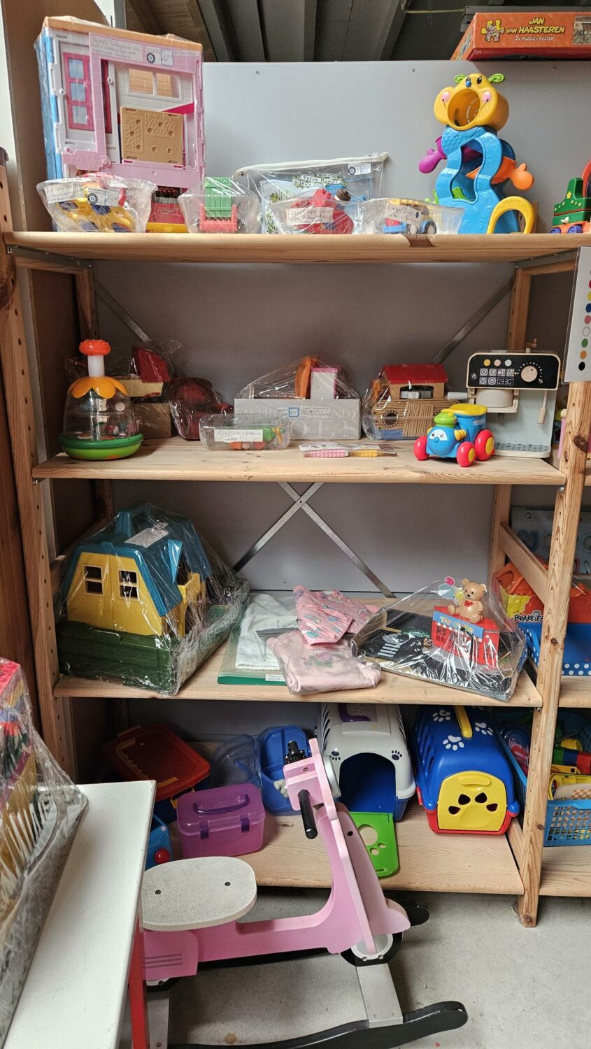 Speelgoed en kinderartikelen op een houten plankenkast, symboliseert hulp en ondersteuning voor kinderen in noodgebieden, passend bij de missie van Dorcas voor humanitaire hulp.