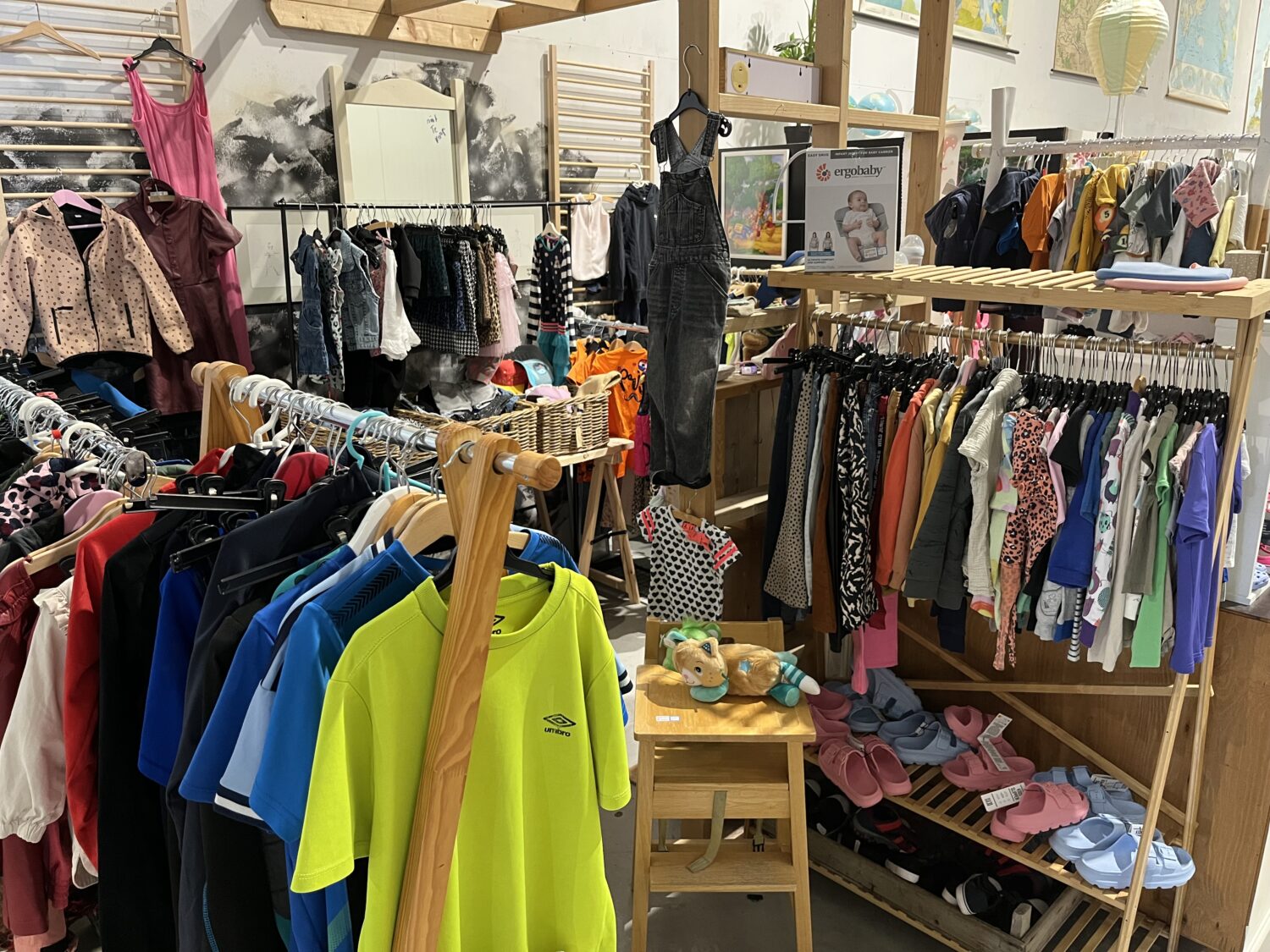 Tweedehands kinderkleding en schoenen in een winkel, gericht op humanitaire hulp en armoedebestrijding, met diverse kledingstukken en schoenen op houten rekken en planken.