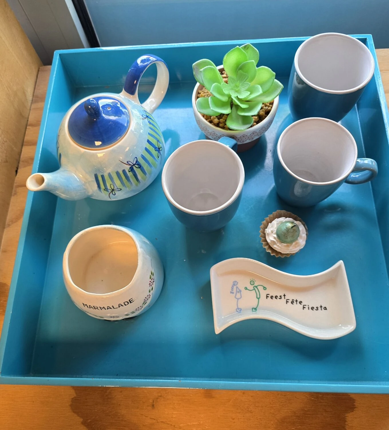 Kleurrijk theeservies met kopjes, een theepot, een plant en een schaal met tekst, symboliseert gezelligheid en samen zijn, passend bij de missie van Dorcas voor humanitaire hulp en armoedebestrijding.