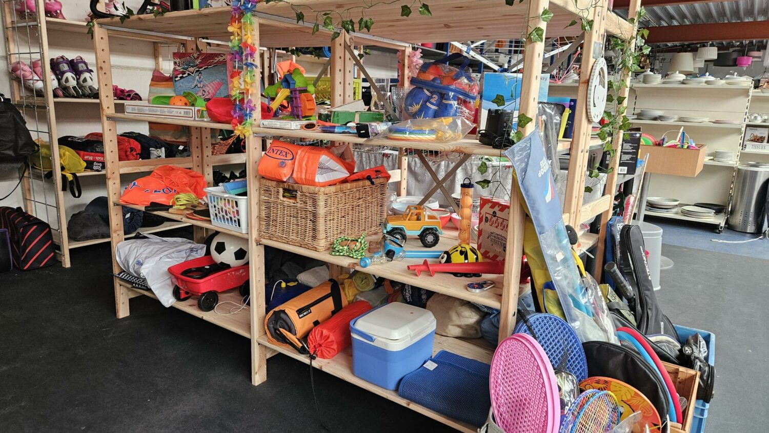 Diverse tweedehands spullen en speelgoed op houten rekken, klaar voor verkoop of donatie, in een winkel of opslagruimte, passend bij de missie van Dorcas voor humanitaire hulp.