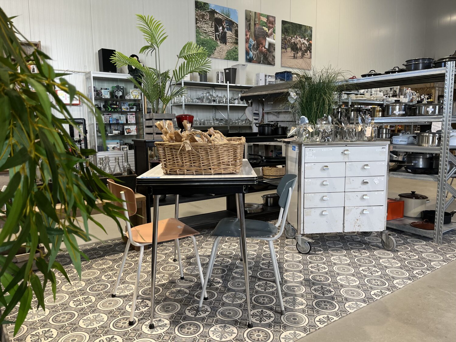 Interieur van een winkel of atelier met een tafel, stoelen, planten en muurdecoraties, gericht op creativiteit en ambacht, passend bij de missie van Dorcas voor humanitaire hulp en armoedebestrijding.