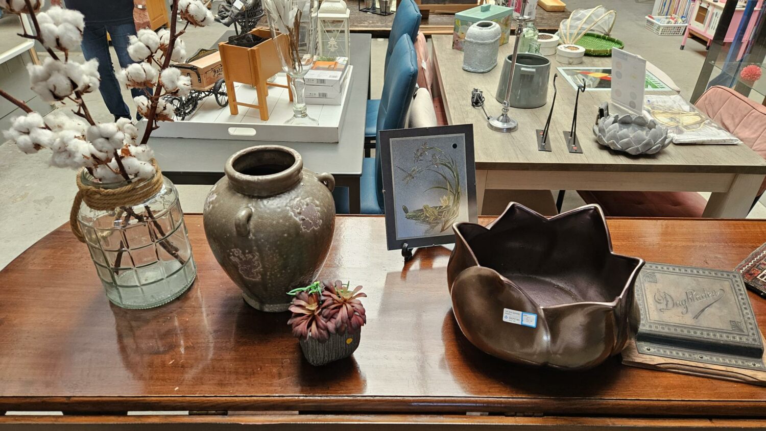 Decoratieve items zoals vazen, een bloemstuk en kunstwerken op een houten tafel, geschikt voor humanitaire hulp en armoedebestrijding, passend bij de missie van Dorcas.