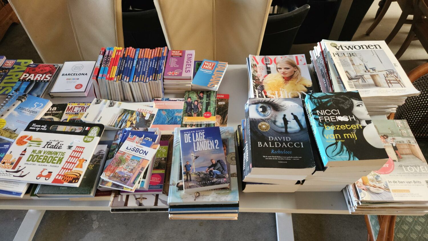 Diverse boeken en tijdschriften over reizen, steden en literatuur liggen op een tafel, klaar voor verkoop of uitwisseling, passend bij de missie van Dorcas voor humanitaire hulp en armoedebestrijding.