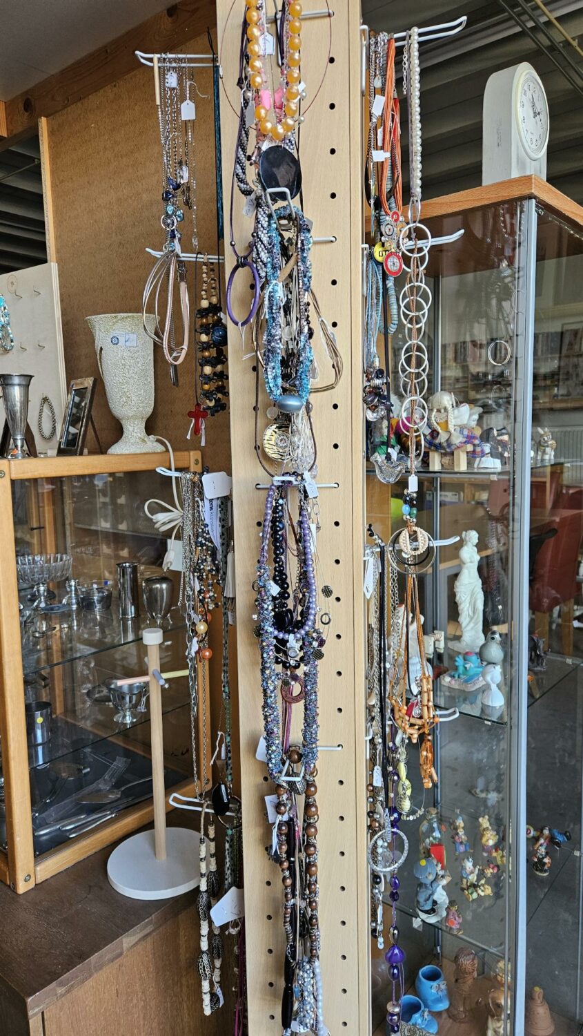 Verschillende sieraden en accessoires hangen aan een houten rek, symboliserend hulp en ondersteuning in humanitaire projecten van Dorcas.