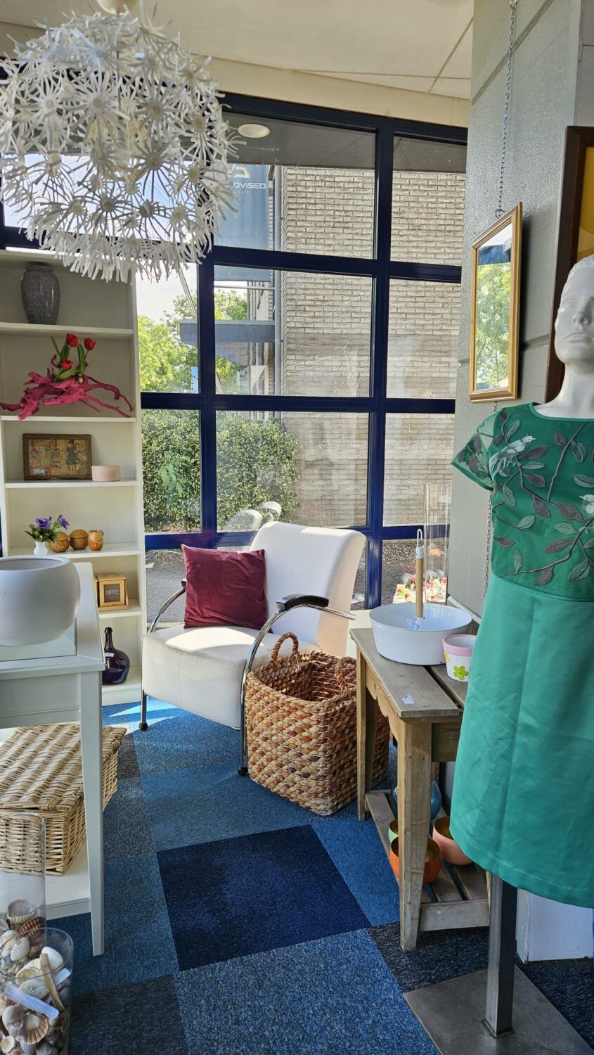 Interieur van een gezellige woonkamer met grote ramen, een witte stoel met kussen, een mand en decoratieve items, passend bij de missie van Dorcas voor humanitaire hulp en armoedebestrijding.