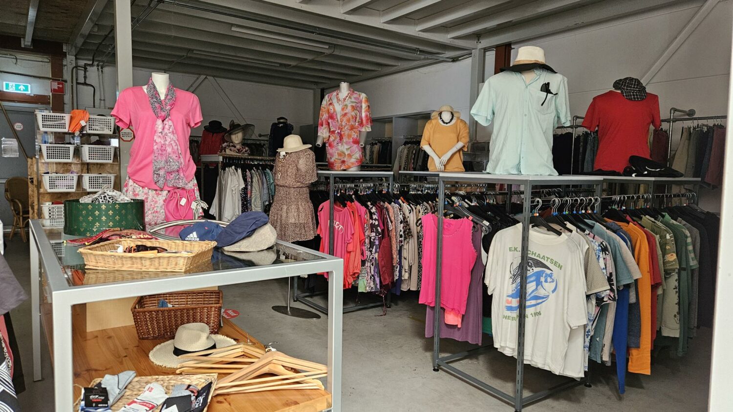 Tweedehands kleding en accessoires bij een liefdadigheidswinkel, gericht op humanitaire hulp en armoedebestrijding, met diverse kledingrekken en tafels vol spullen.