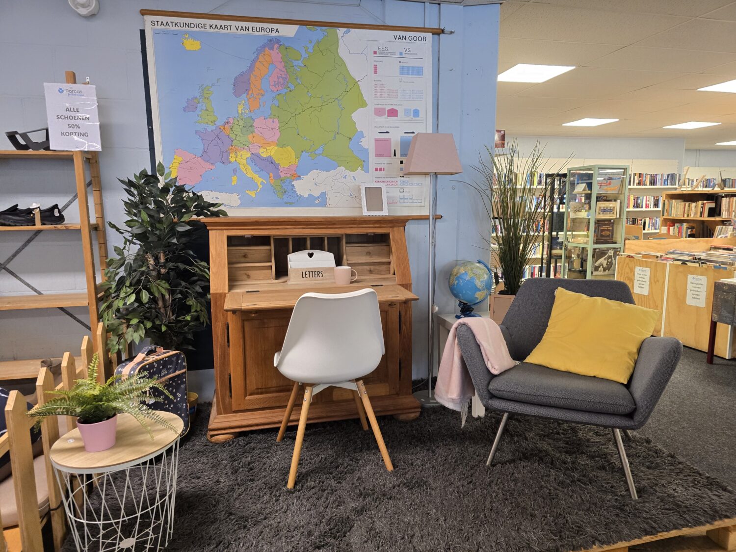Een leeshoek in een bibliotheek met een houten bureau, witte stoel, grijze bank met gele kussen, wereldbol en planten, symboliseert educatie en hulp voor ontwikkelingslanden.