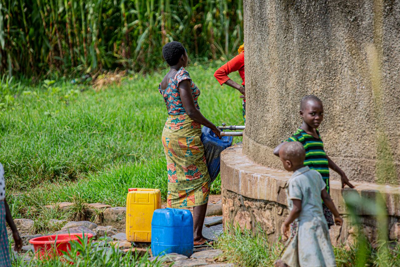 Kinderen en een vrouw vullen water uit een waterpunt in Kenia, symboliseert humanitaire hulp en armoedebestrijding in ontwikkelingslanden.