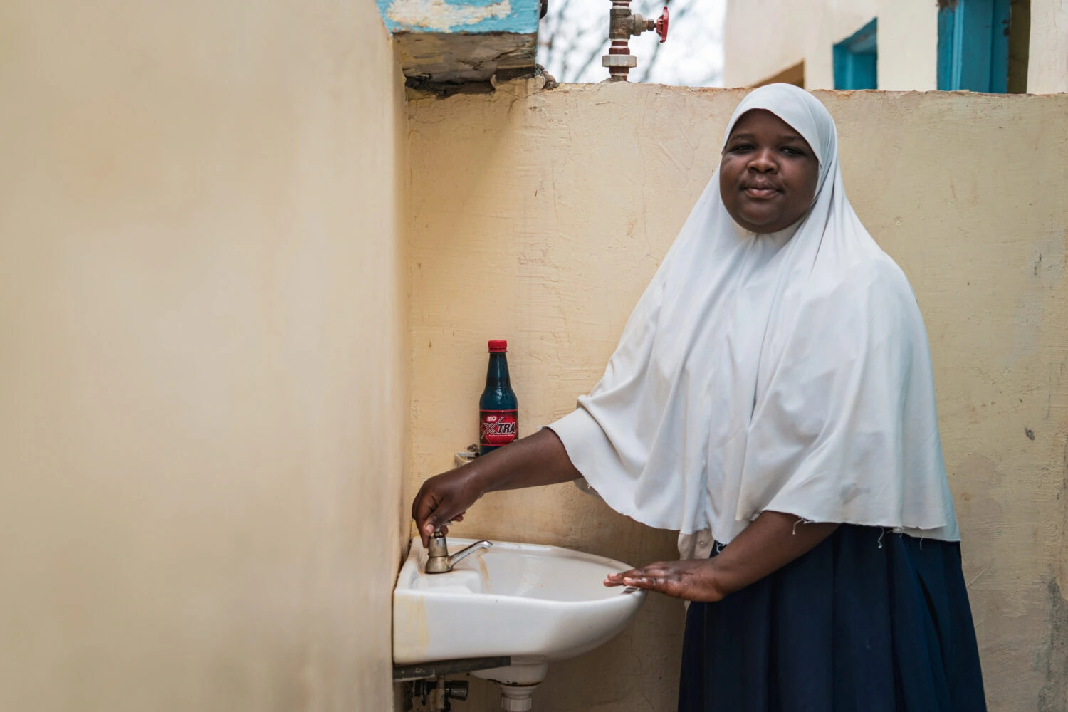 Een vrouw in Tanzania wast haar handen bij een waterkraan, een symbool van humanitaire hulp en armoedebestrijding door Dorcas in ontwikkelingslanden.