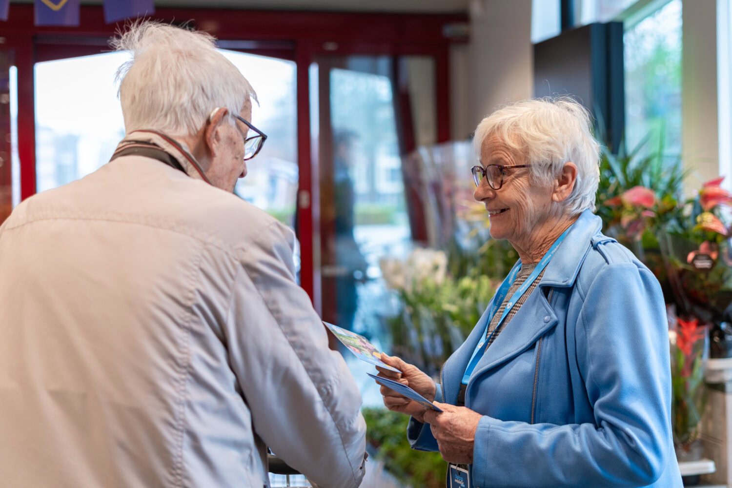Oudere vrouw krijgt hulp van medewerker in winkel, symboliseert humanitaire hulp en zorg voor kwetsbaren, passend bij missie van Dorcas in noodhulp en armoedebestrijding.