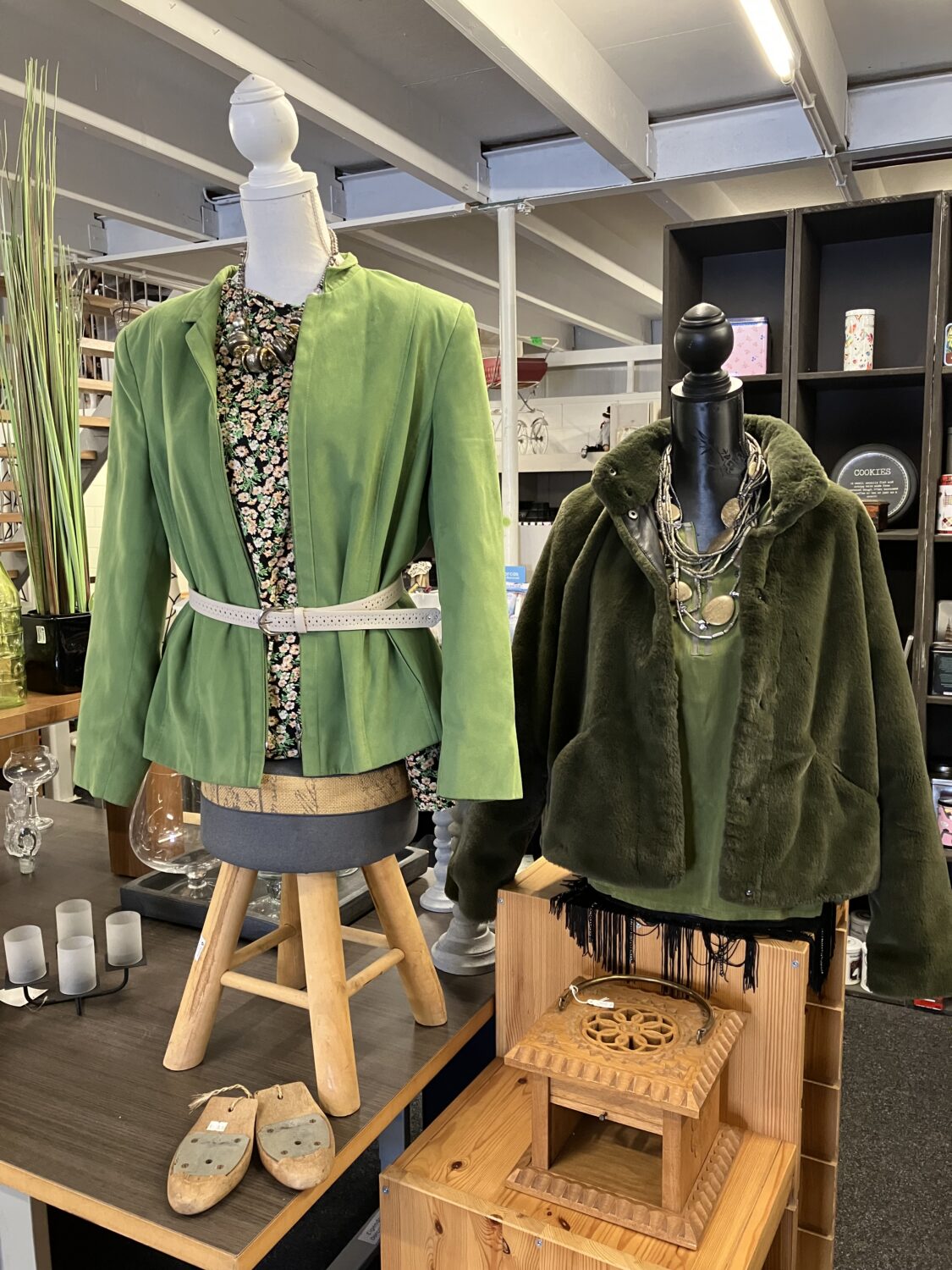 Dameskleding op mannequins in een winkel, met groene jas en blouse, symboliseert duurzame mode en humanitaire hulp, passend bij Dorcas' missie voor armoedebestrijding en noodhulp.