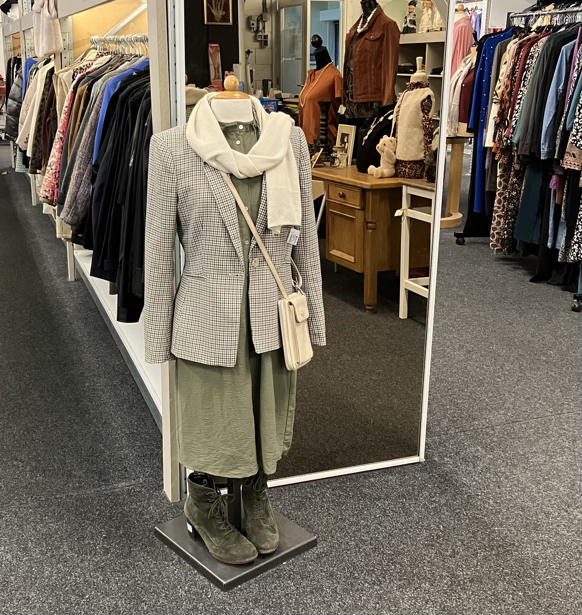 Modieuze damesoutfit op mannequin in kledingwinkel met diverse kledingrekken op achtergrond, gericht op armoedebestrijding en humanitaire hulp.