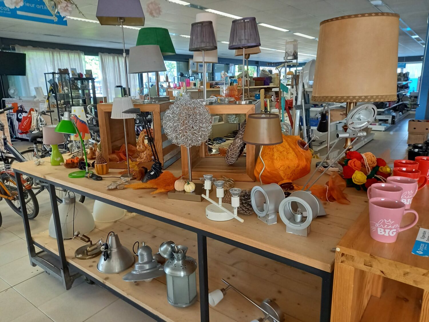 Diverse tweedehands lampen en accessoires op een tafel in een kringloopwinkel, gericht op hergebruik en armoedebestrijding.