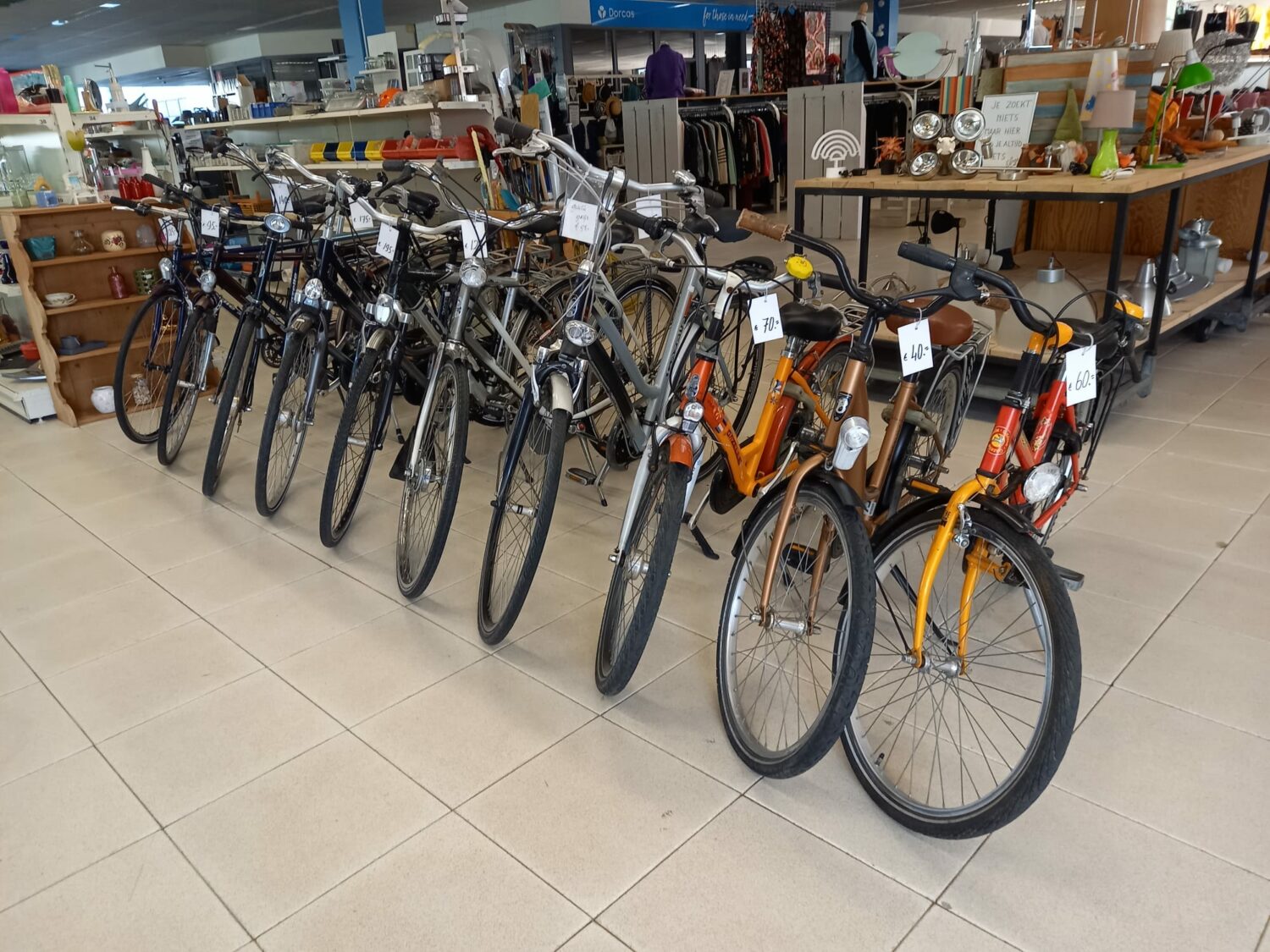 Verschillende fietsen staan in een winkel, klaar voor verkoop, met achtergrond van winkelrekken en kleding. Ideaal voor duurzame mobiliteit en armoedebestrijding.