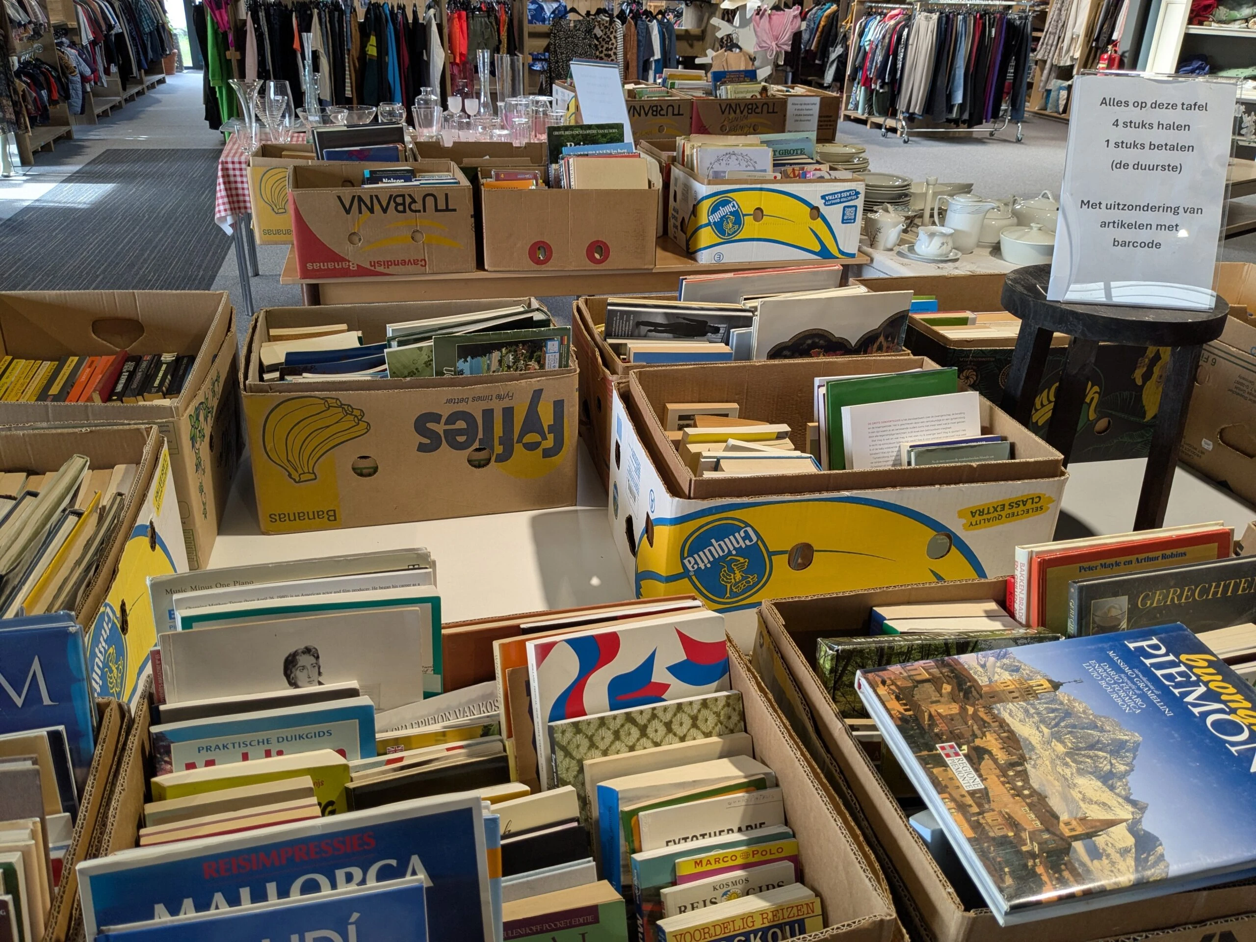 Tweedehands boeken en spullen op een rommelmarkt, met diverse kasten en tafels vol boeken en huishoudartikelen, geschikt voor humanitaire hulp en armoedebestrijding.