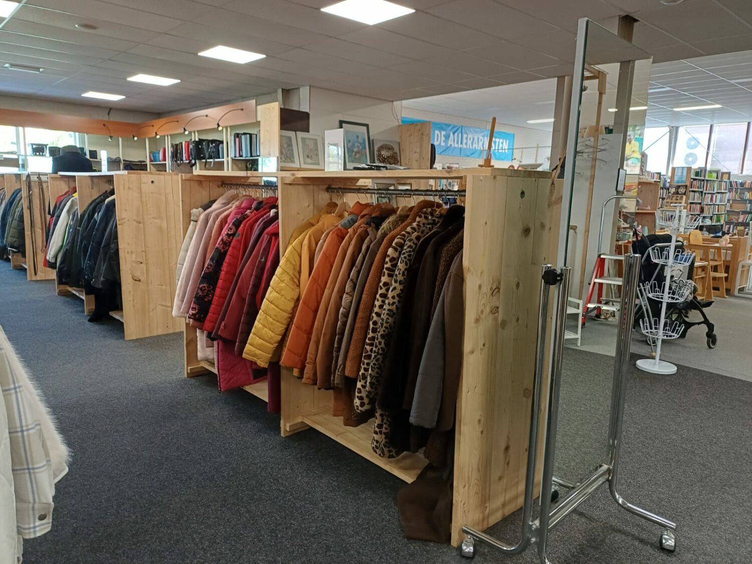 Kledingrekken met warme jassen en kleding in een bibliotheek of gemeenschapscentrum, onderdeel van humanitaire hulp en armoedebestrijding door Dorcas.