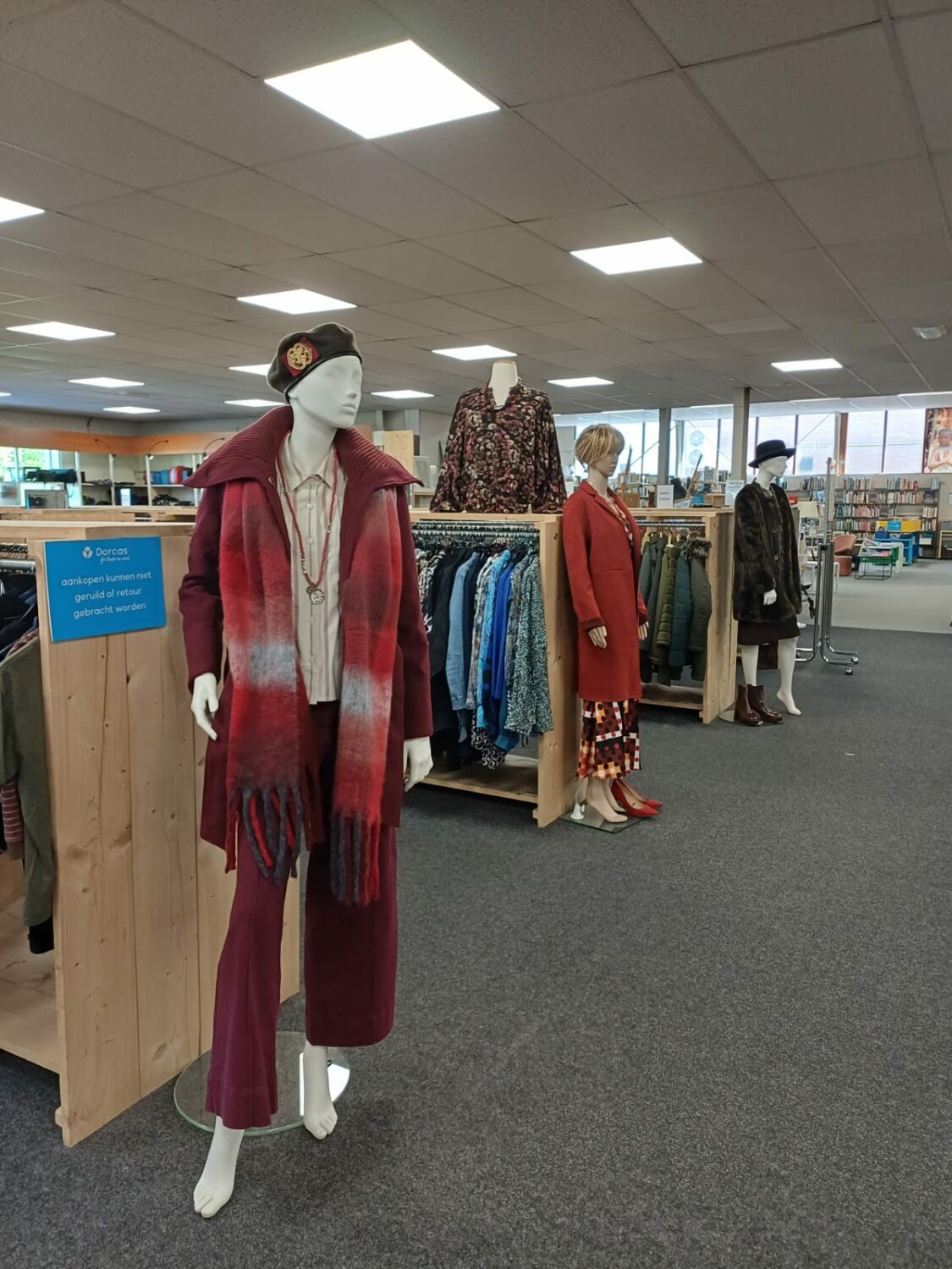 Mannequin in kledingwinkel met winteroutfit, inclusief rode jas en sjaal, symboliseert humanitaire hulp en armoedebestrijding door Dorcas in Oost-Europa, Oost-Afrika en het Midden-Oosten.