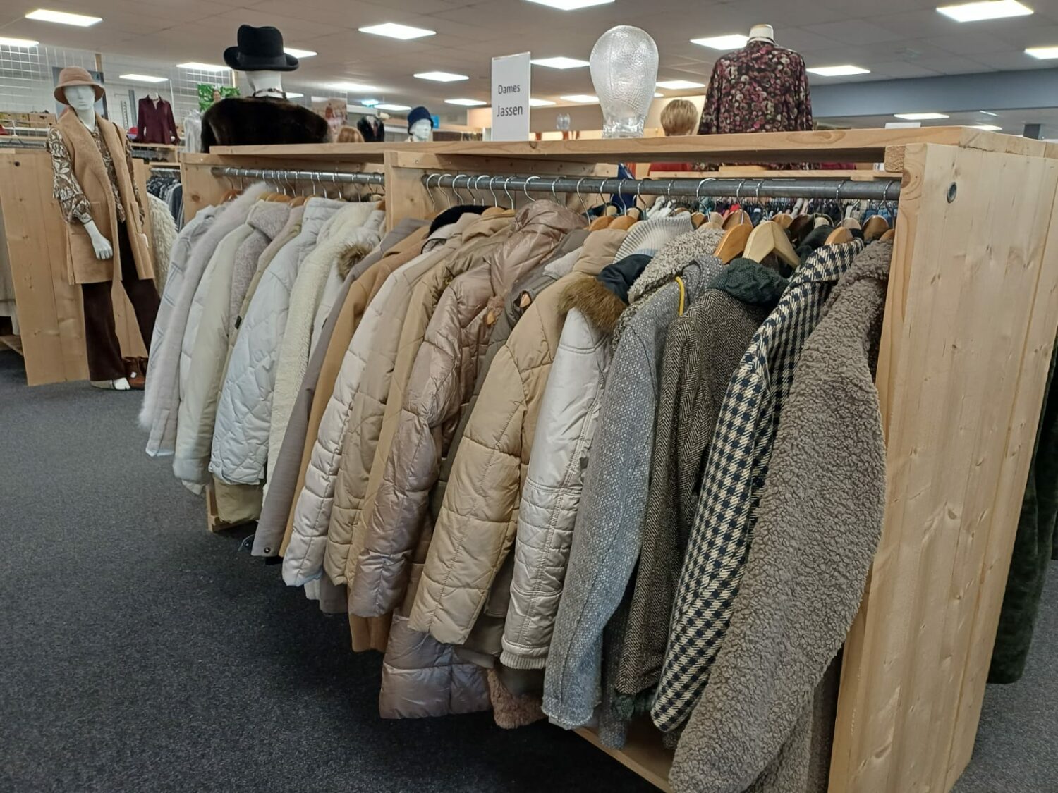 Kledingrek met winterjassen en wollen vesten in een winkel, geschikt voor humanitaire hulp en armoedebestrijding, benadrukt noodhulp en ontwikkelingssamenwerking.